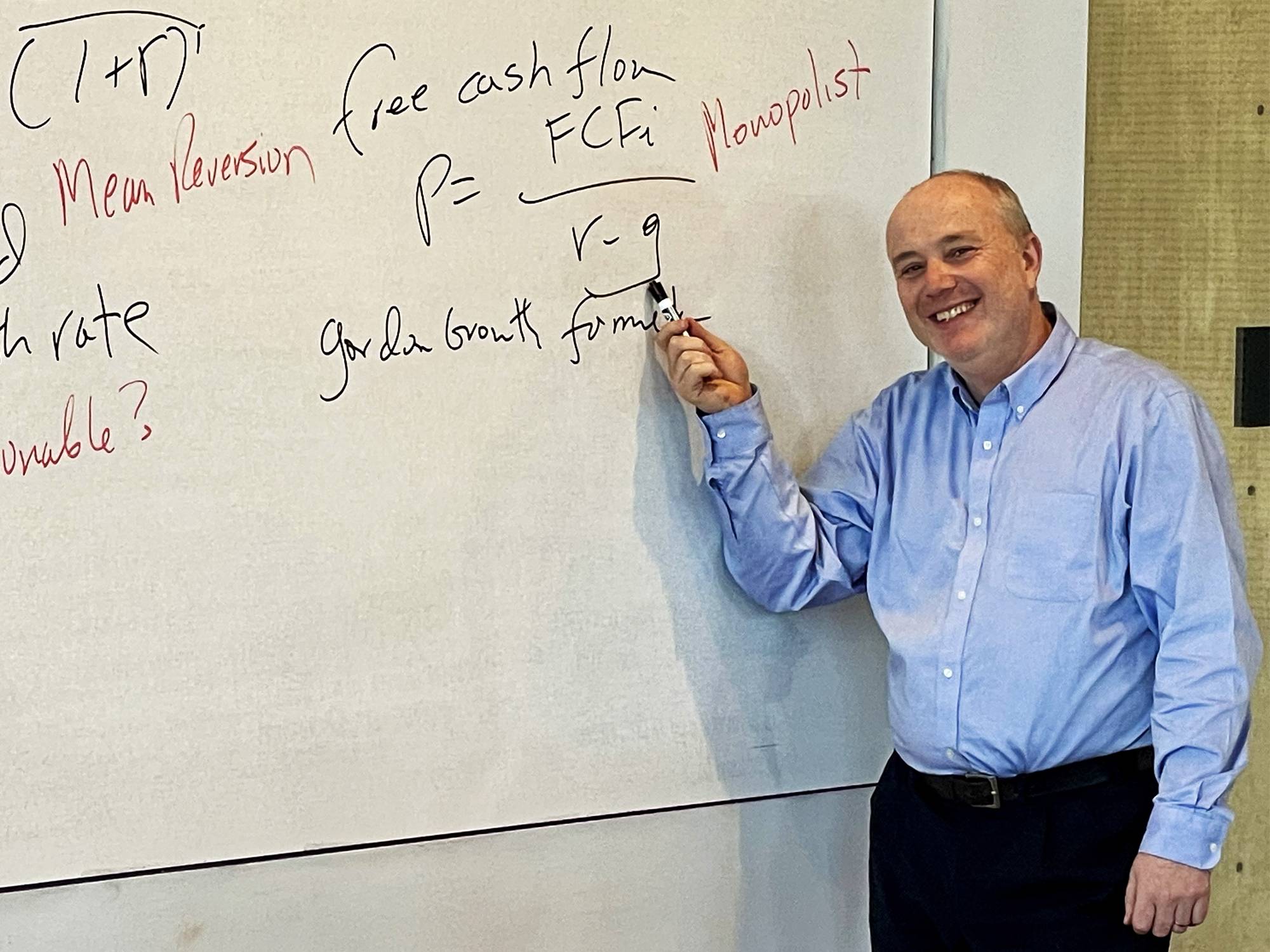 Mikhail Pevzner, Ph.D. standing in front of a classroom's whiteboard pointing to financial formulas