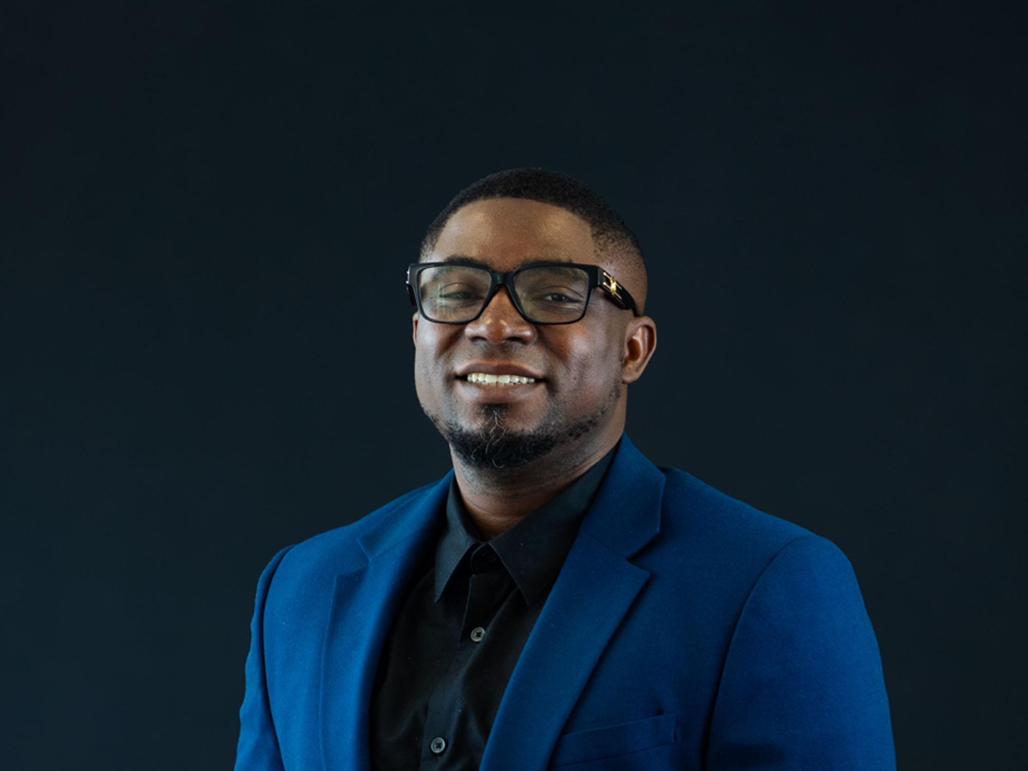 Martins Awofadeju poses in a blue suit on a dark background