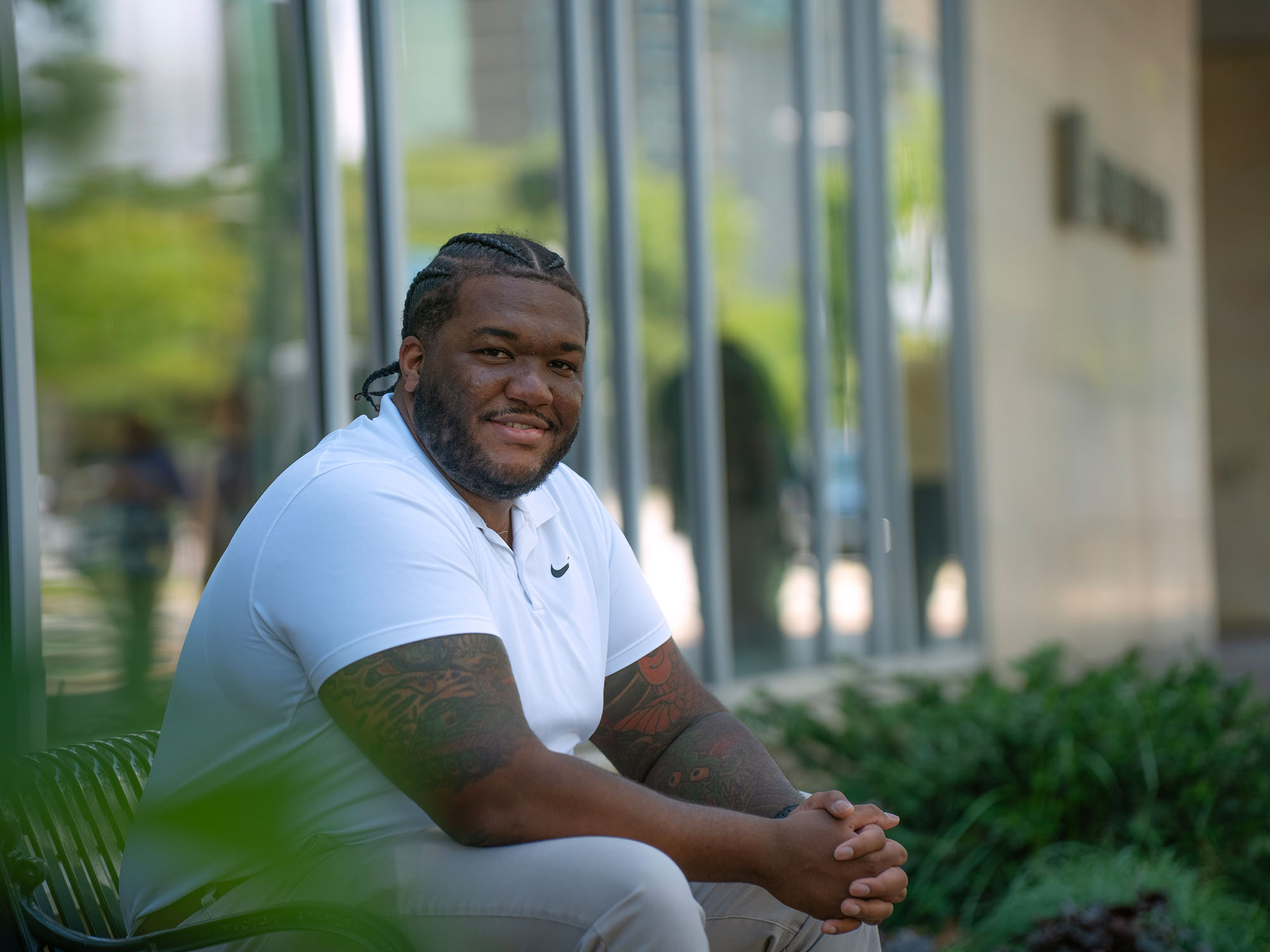 Philip, an undergraduate student, smiles while sitting on a bench outside of the Student Center at The University of Baltimore campus.