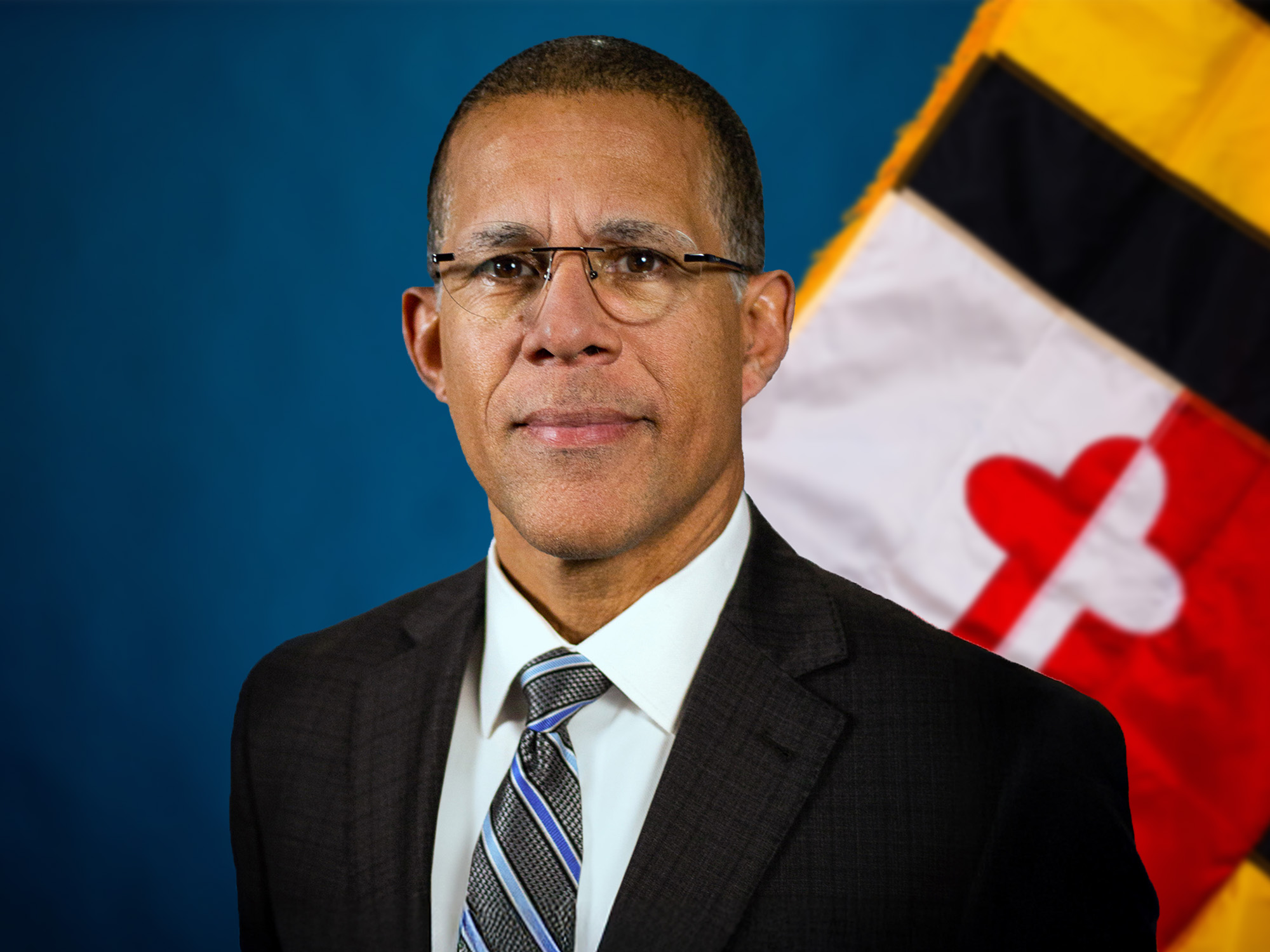 The Honorable Anthony G. Brown tanding in front of a blue background with the Maryland state flag