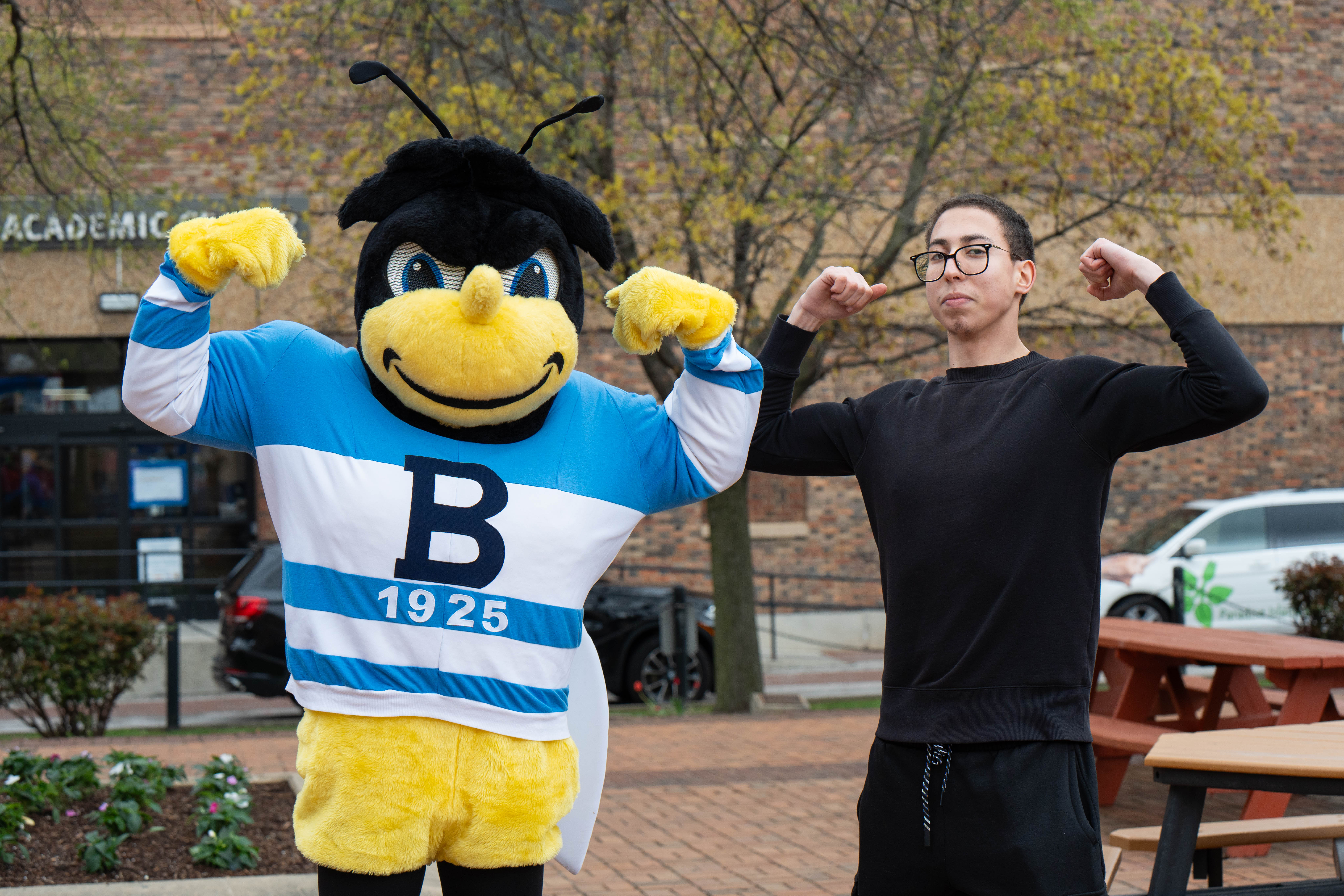 Adam Abidi, a student, poses by flexing with Eubie, the bee mascot, doing the same.