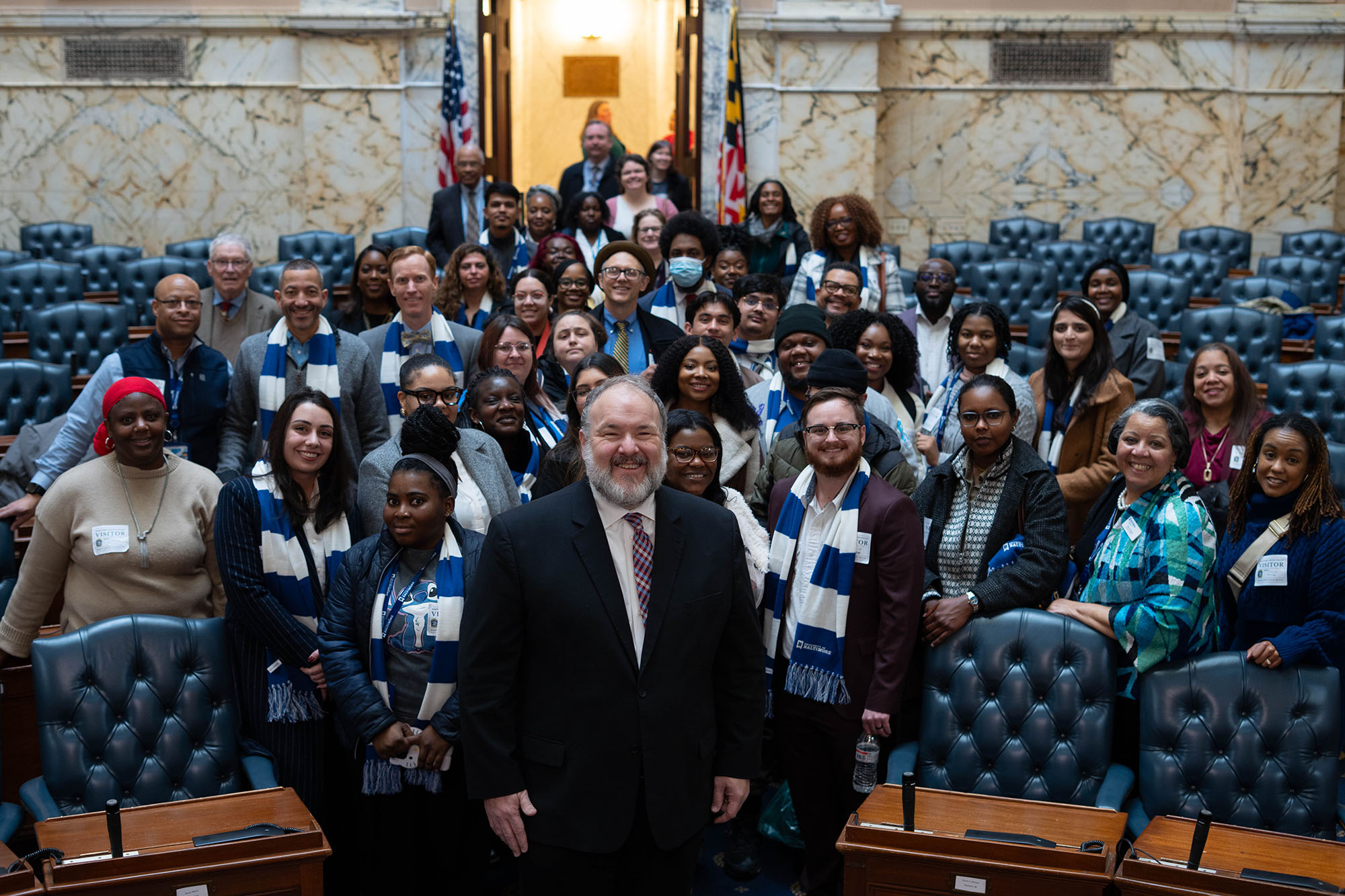 A delegate stands at the center of a large group posing for a photo in the Maryland House chamber. 