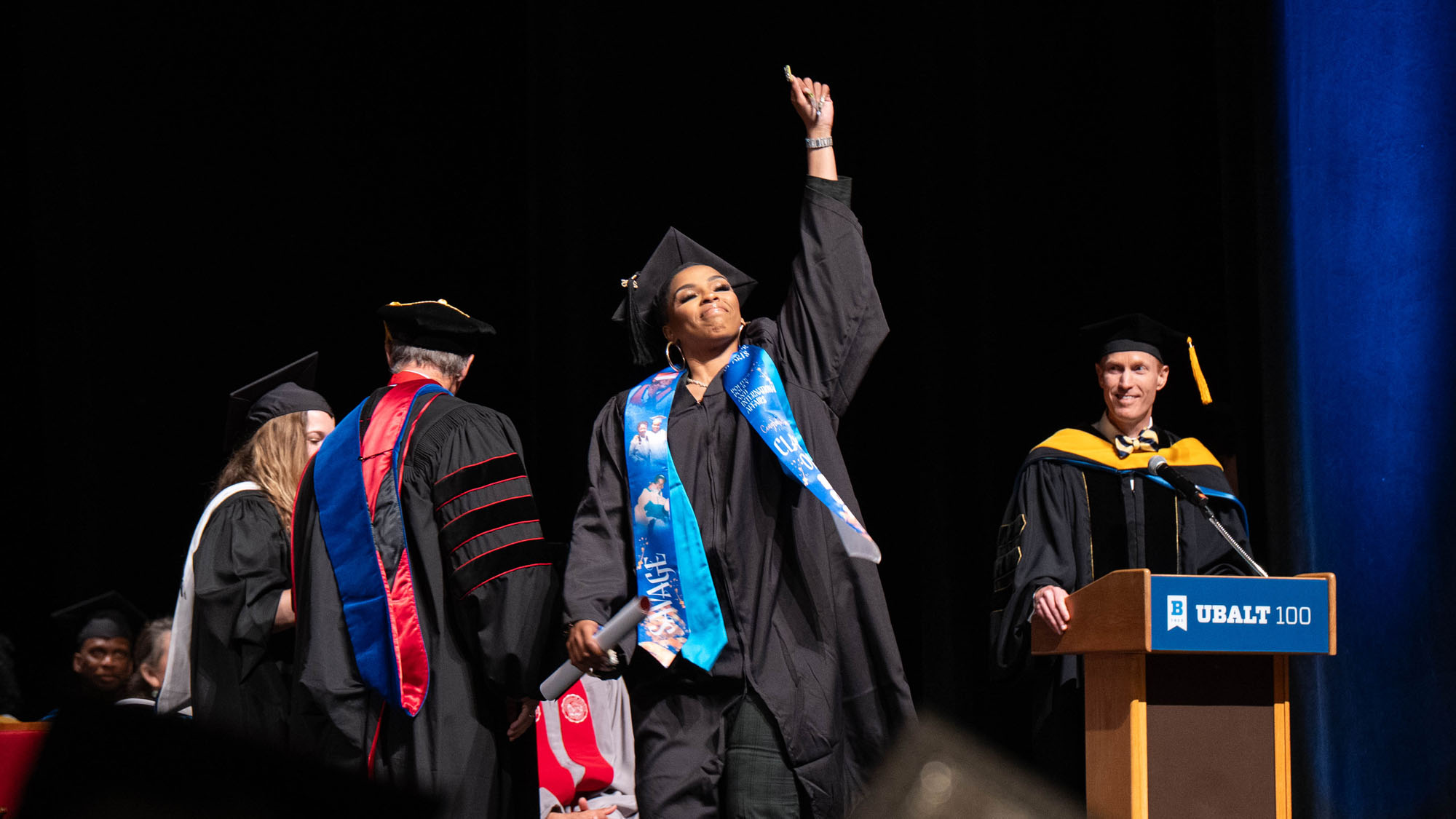 A graduate points to the sky as she walks across the stage. 