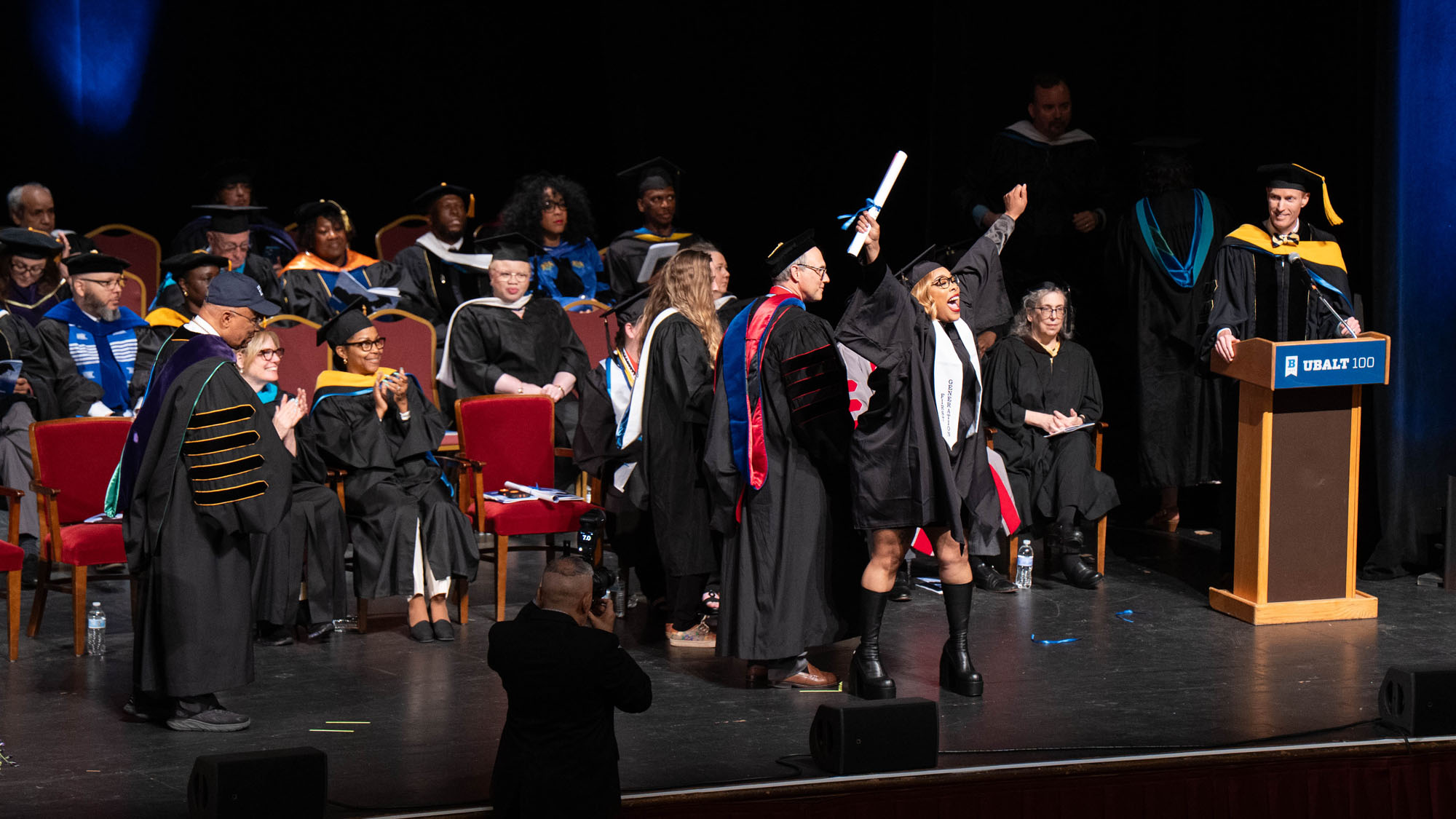 A student raises their hands and screams in excitement over receiving their degree.