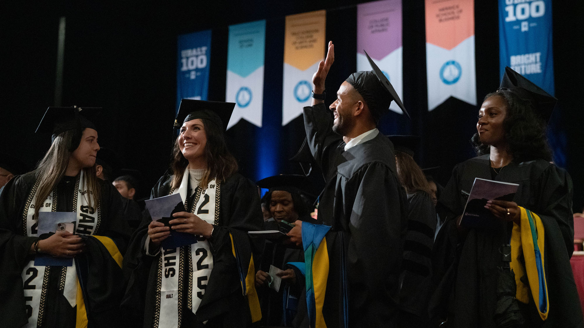 A graduate waves to someone off camera during commencement.