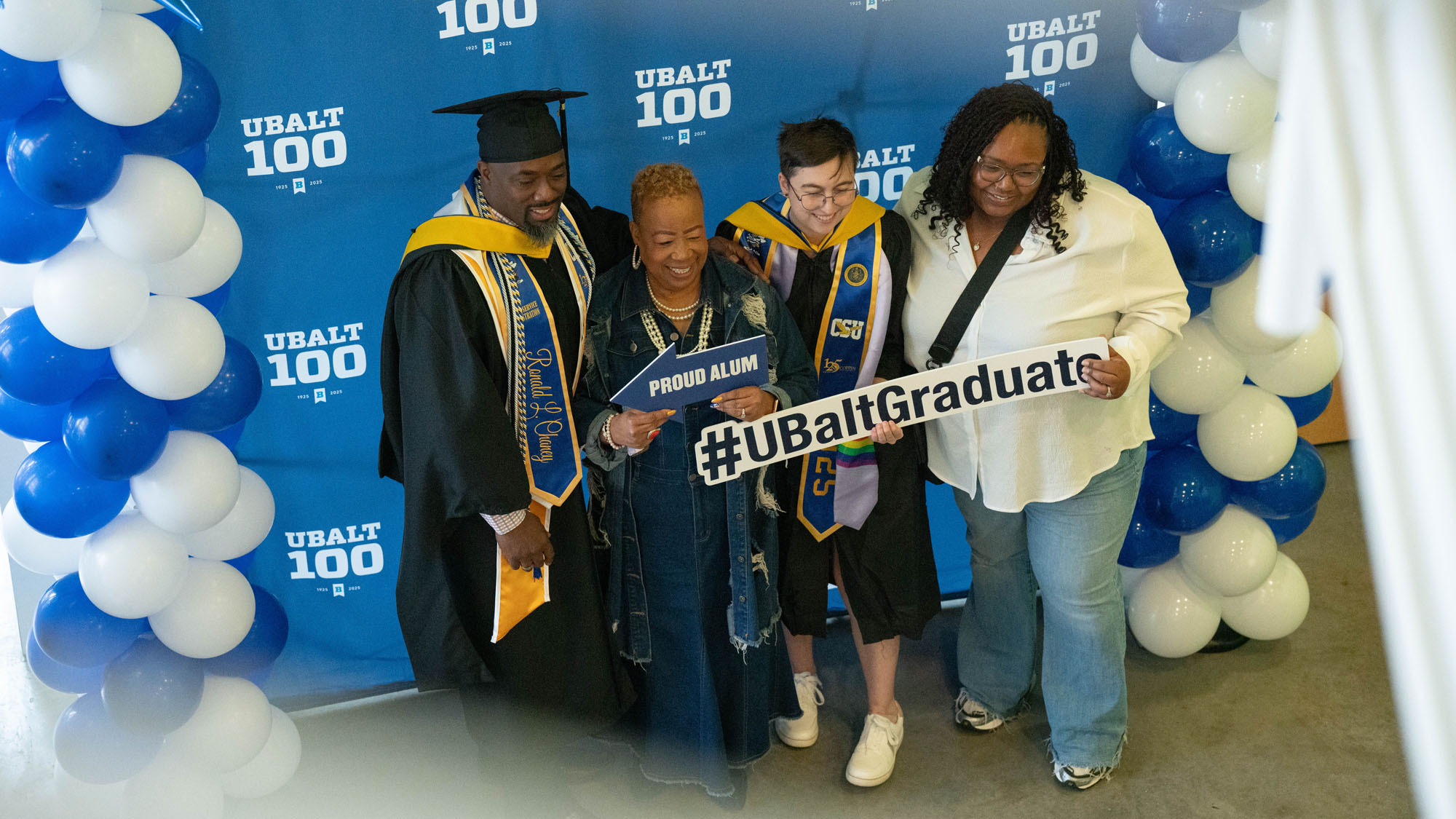Graduates pose for a photo in front of a UBalt backdrop.