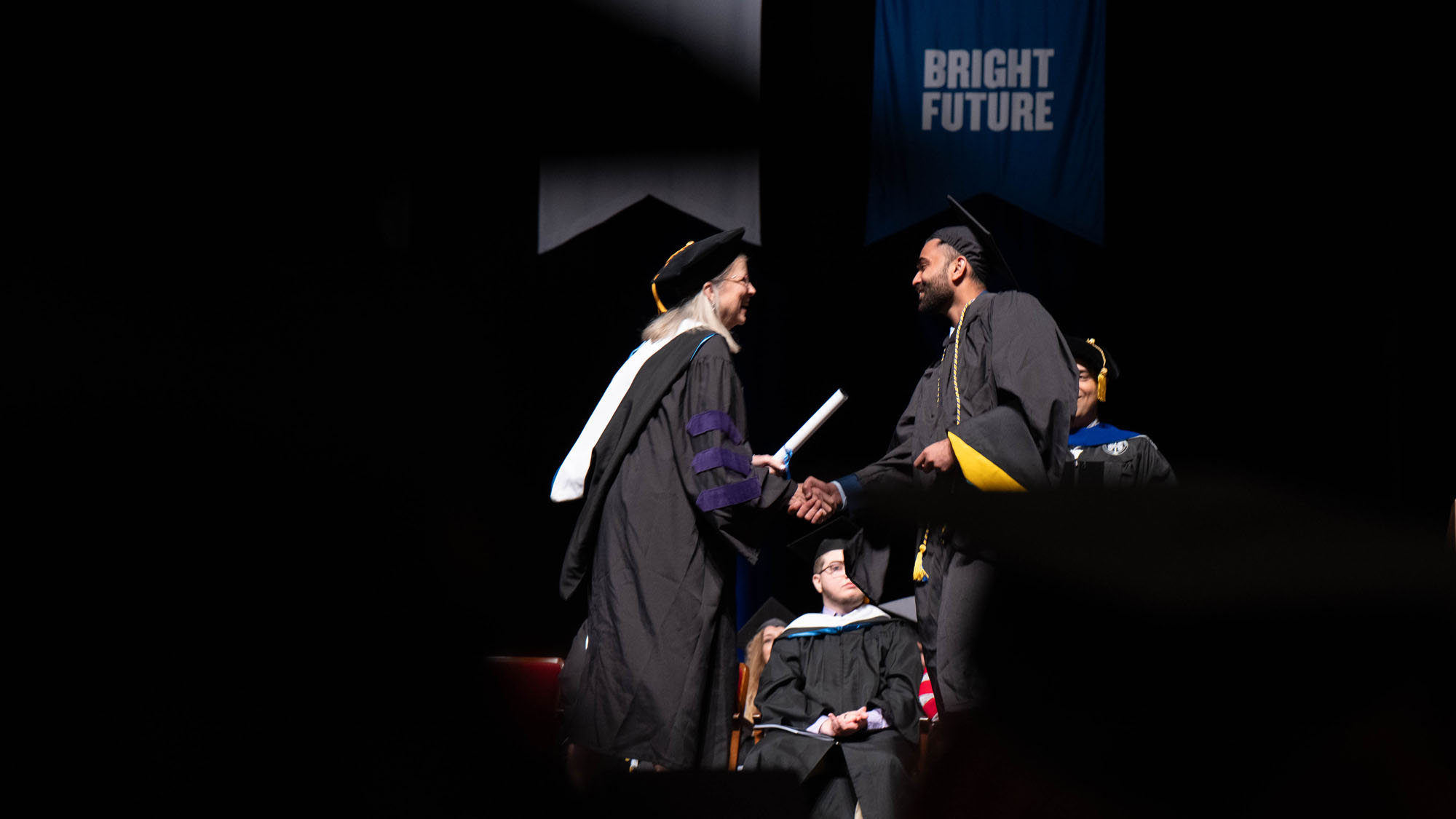 A student shakes hands with faculty as they receive their diploma.