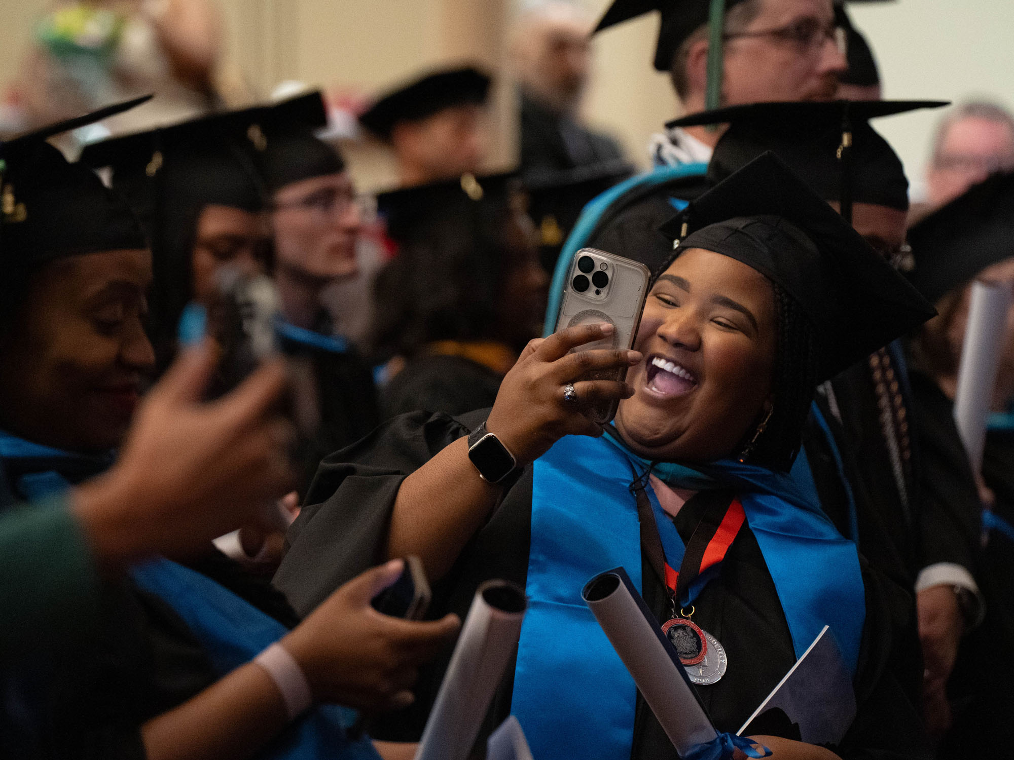 A graduate smiles while taking a selfie during the commencement ceremony at The University of Baltimore.