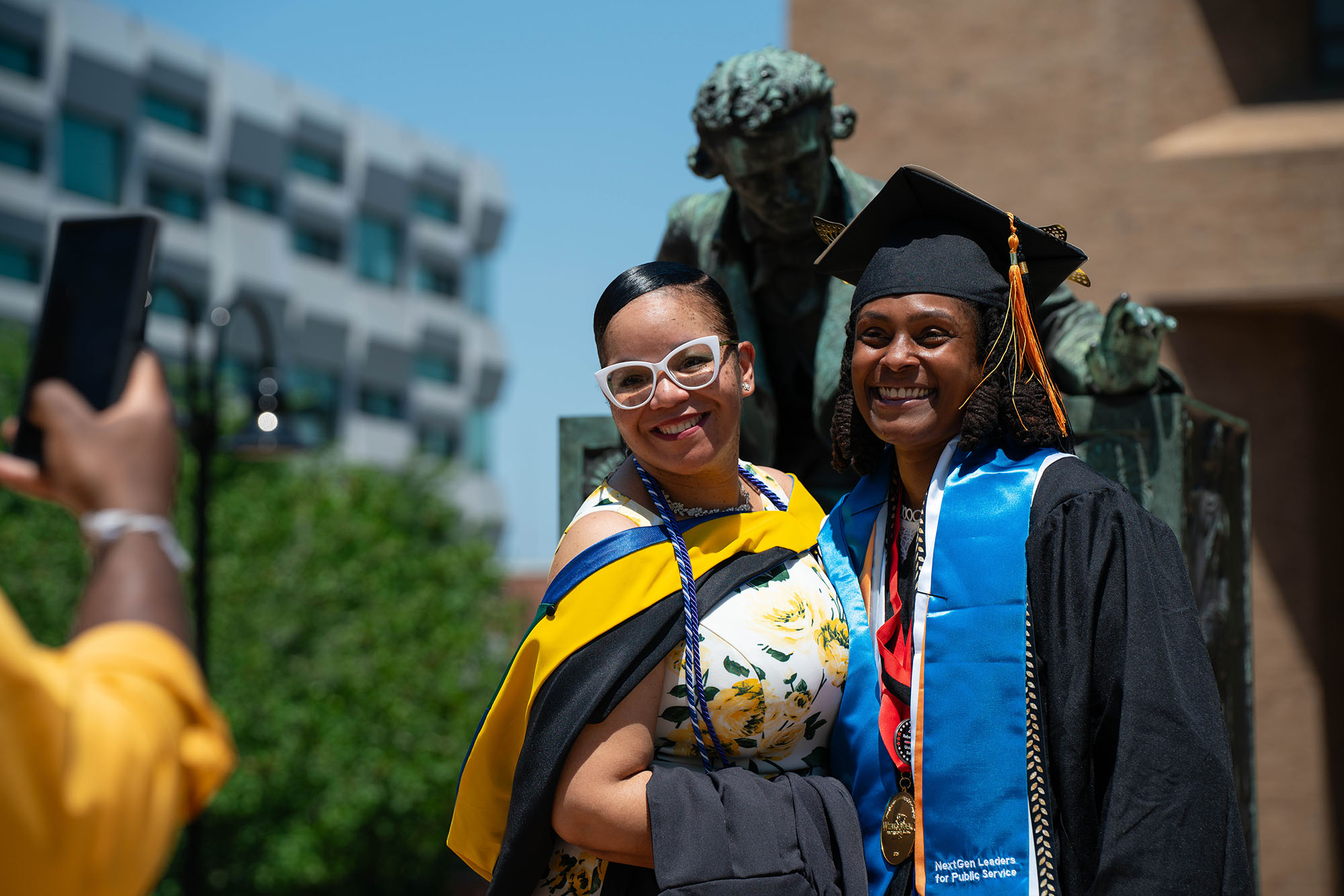 Two graduates pose in front of the Edgar Allen Poe statue at The University of Baltimore.