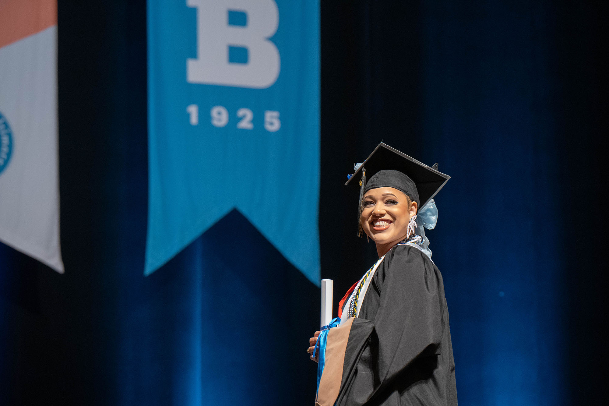 A graduate smiles at the audience after receiving her diploma on the stage at commencement.