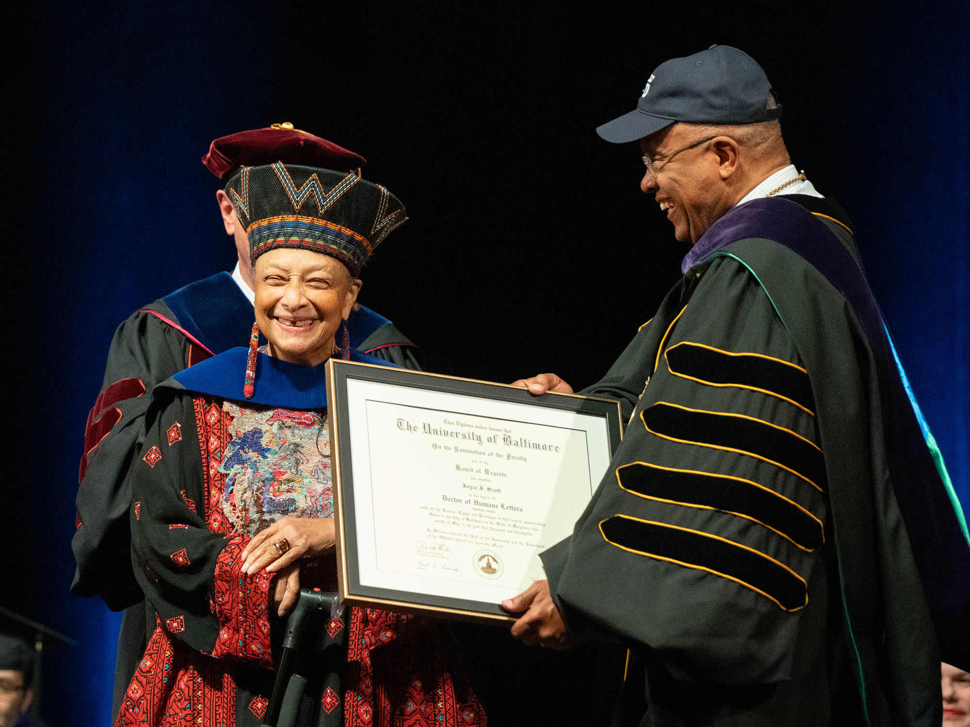 An honorary degree recipient smiles as she is handed her framed degree. 