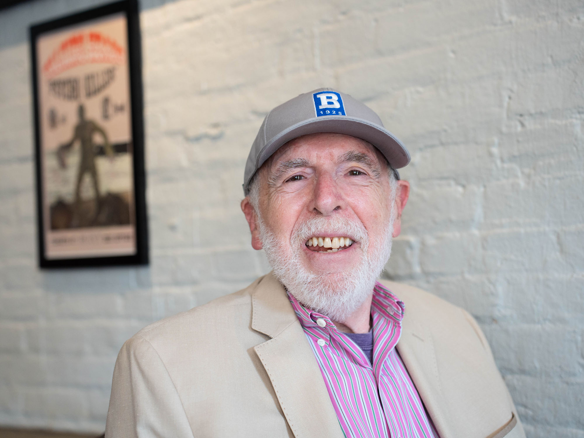 Joseph Adler smiles while sitting in a cafe and wearing a UBalt hat.