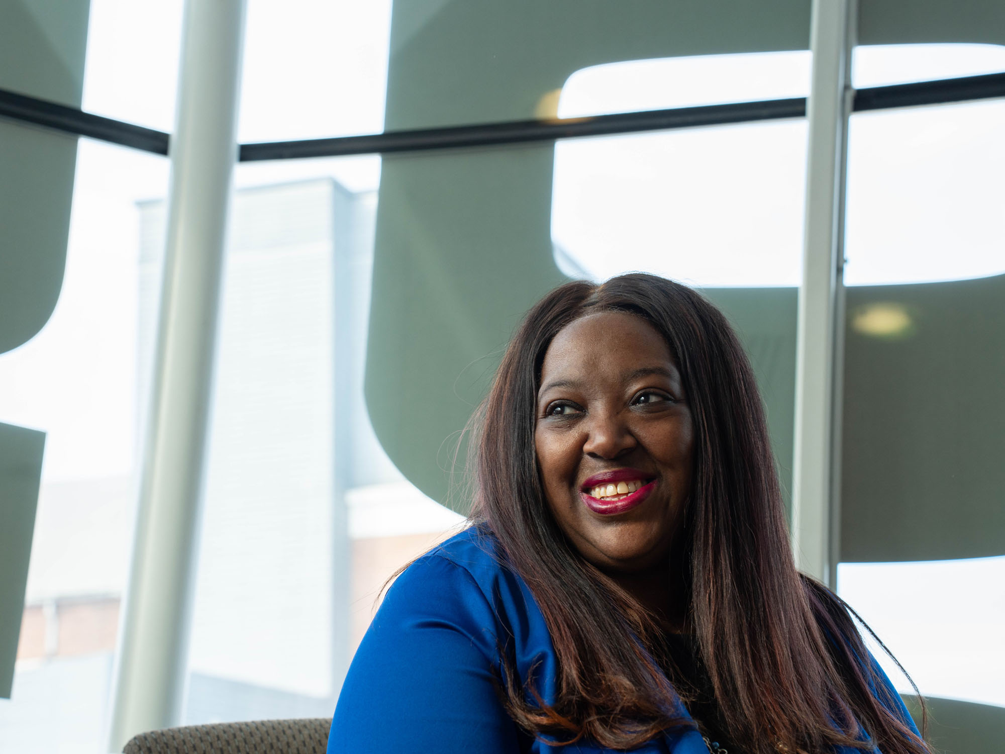 LaToya Gomez smiles while looking away from the camera. She sits in front of windows. 