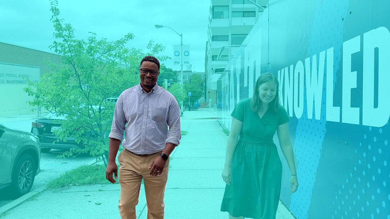 Carey, a UBalt staff member, is highlighted in a color-washed graphic while walking up a Baltimore street with an interviewer.