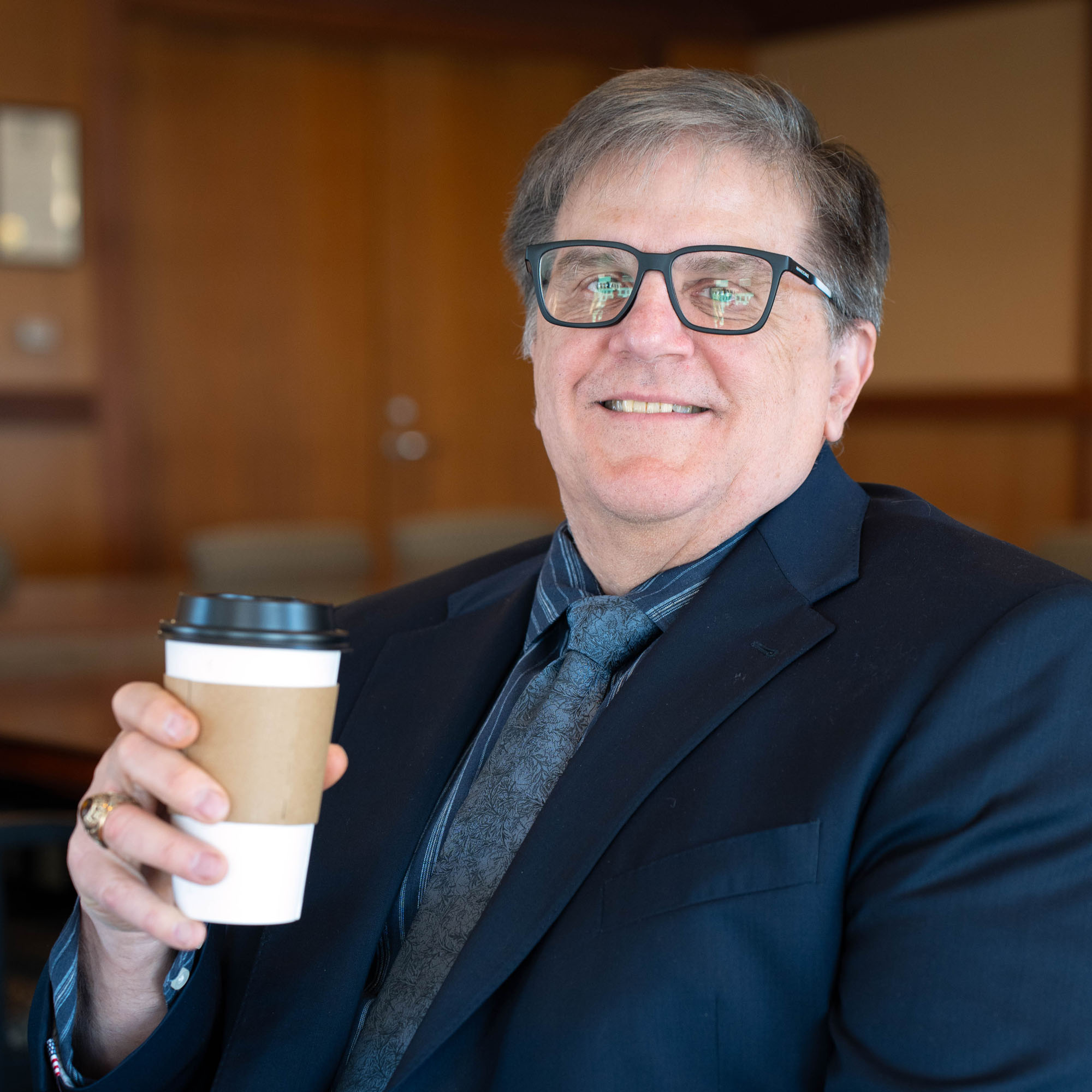 Dan Gerlowski sits holding a coffee cup while smiling at the camera.