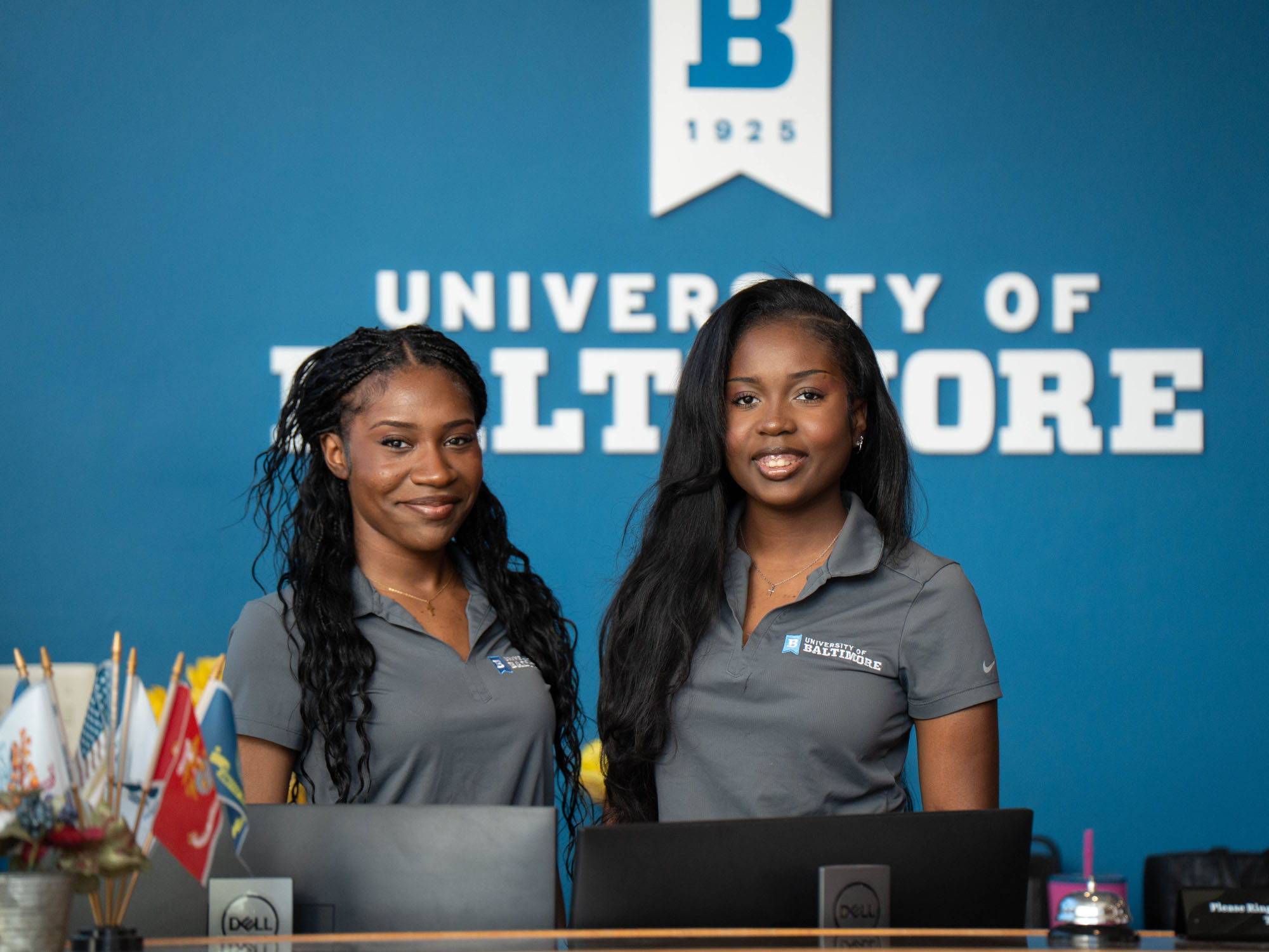Two students stand at the Welcome Center front desk where they serve as student ambassadors for visitors.