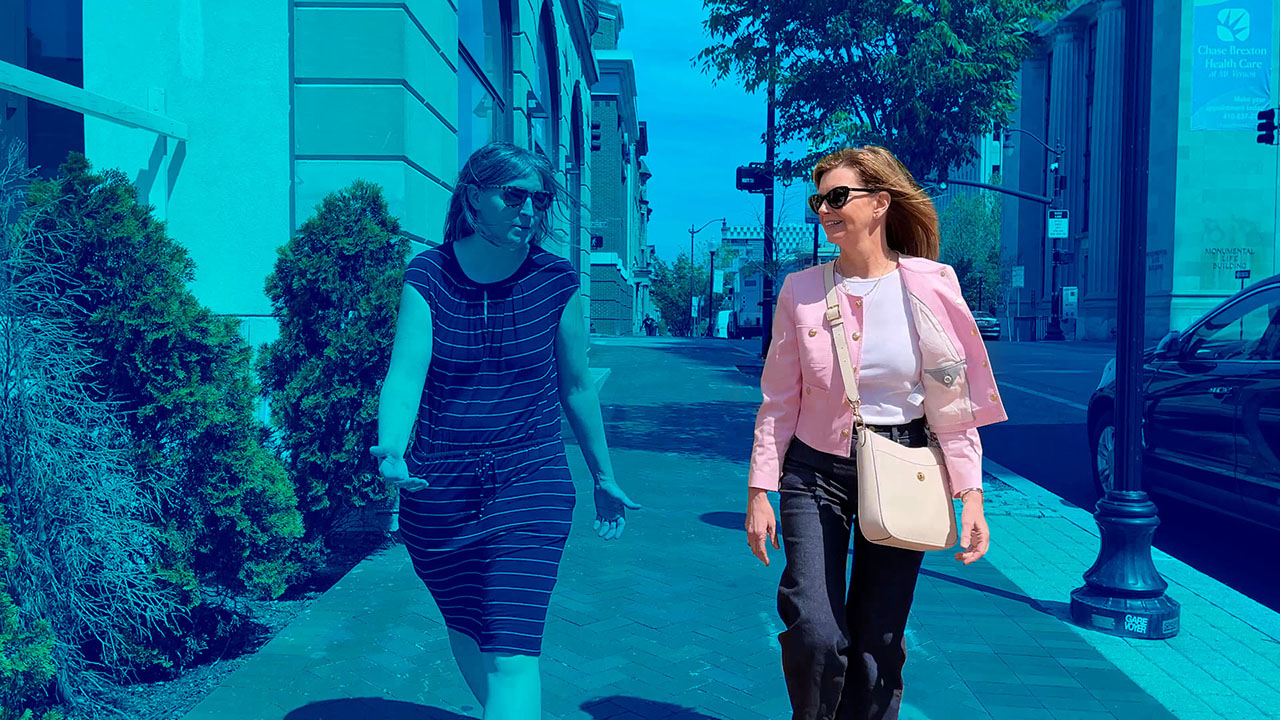 Dionne Koller, a faculty member, is spotlighted in a red-colored still as she's talking and walking up a street.