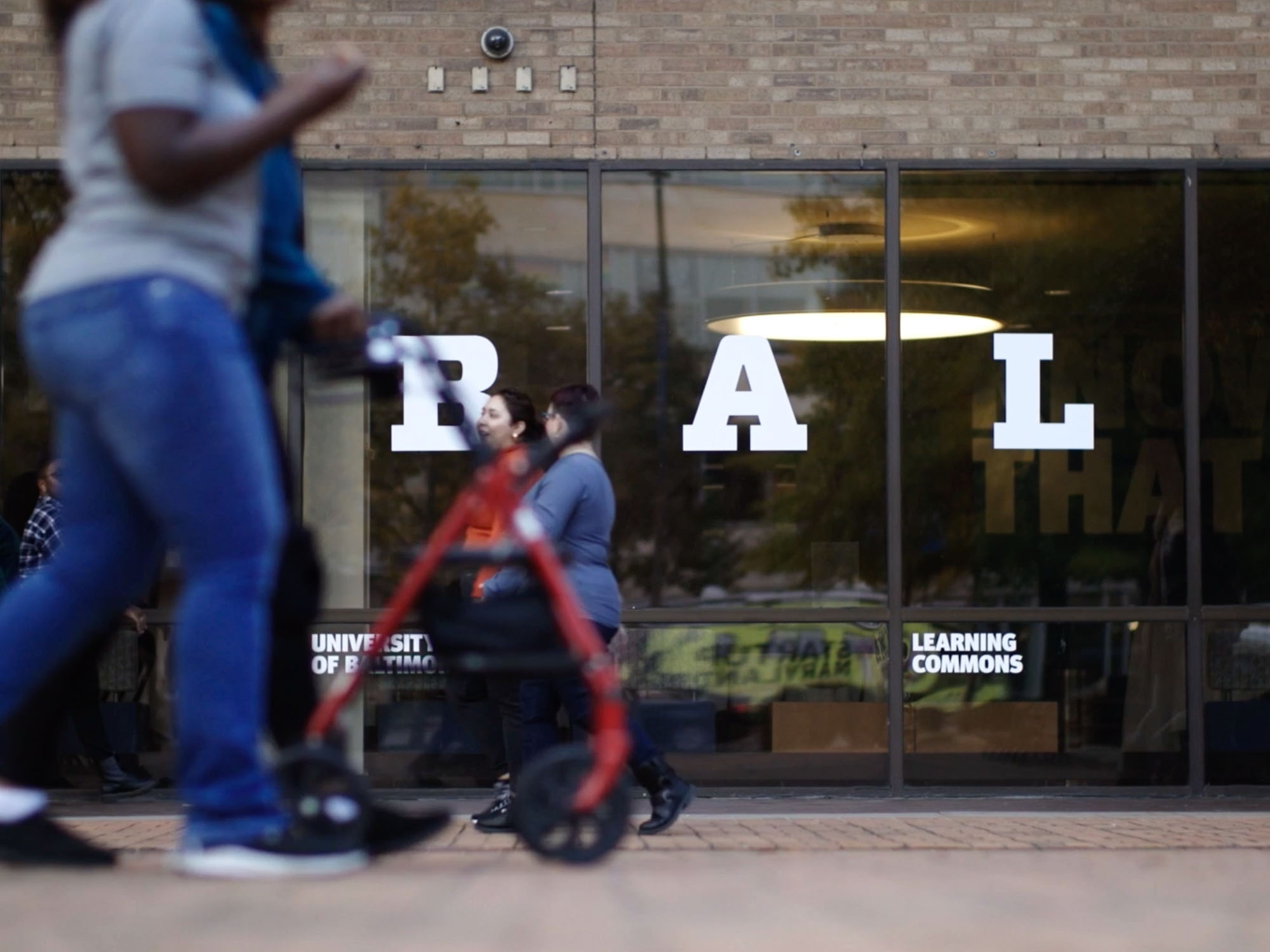 Students walk on campus in front of a building that reads UBALT.