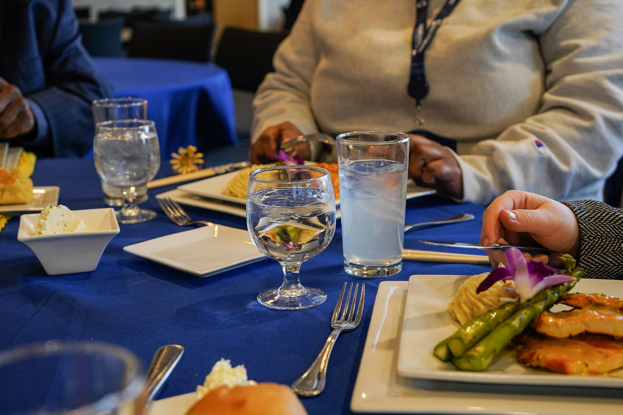 The table is set with food-filled plates and water-filled glasses for an etiquette dinner.