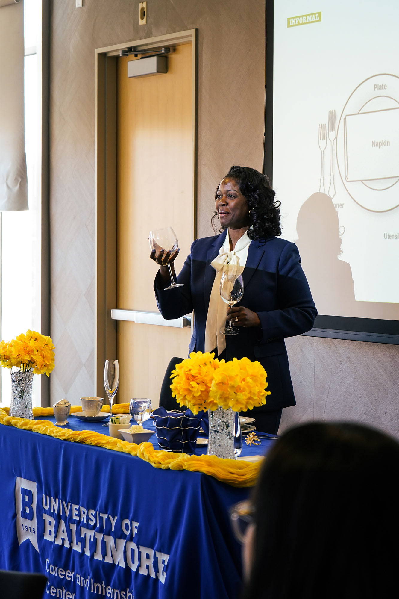 The etiquette dinner host holds two glasses as part of a demonstration. 