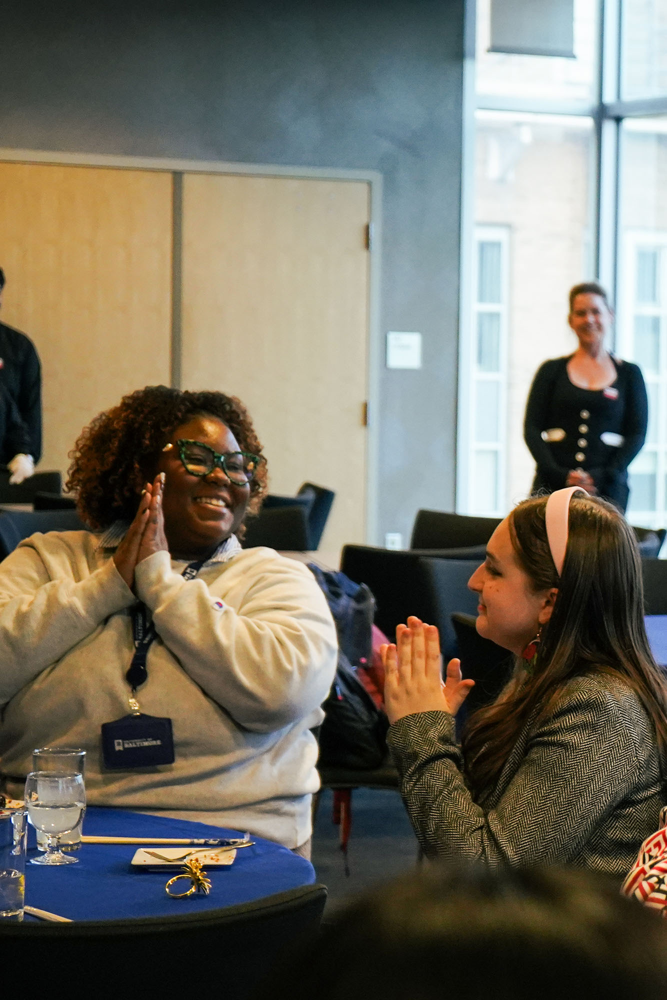 Students applaud while sitting at a table during an event.