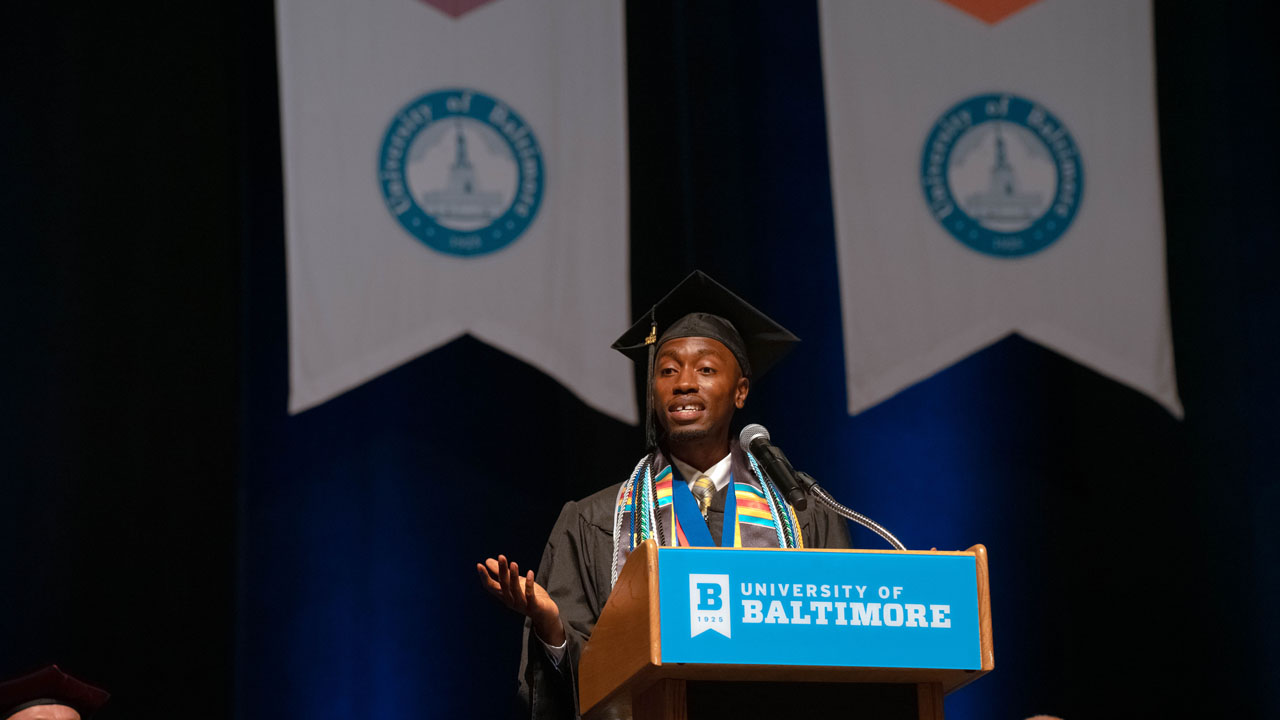 Gamar Hayles gestures while giving his commencement speech at the podium.