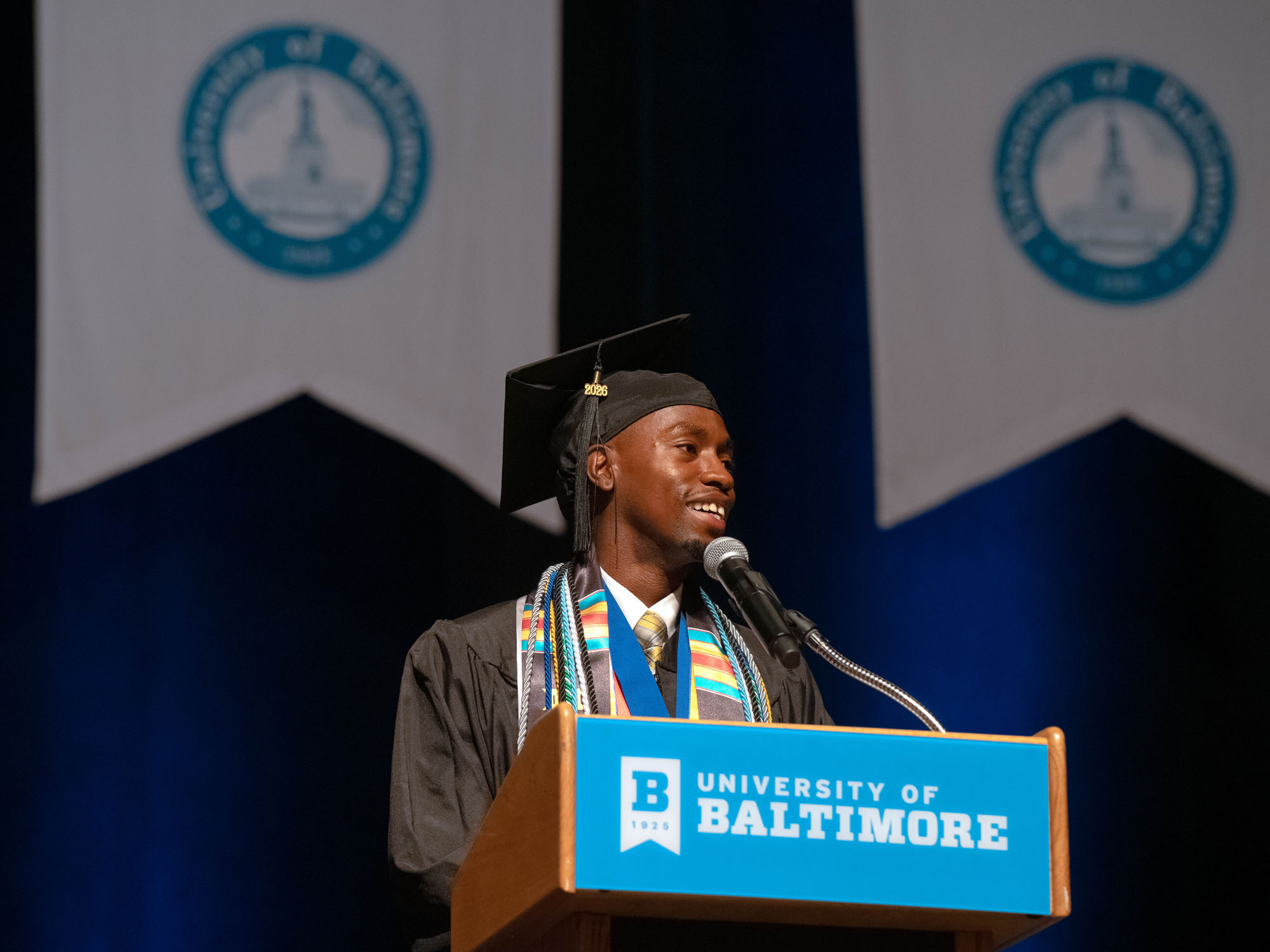 Gamar Hayles speaks from the commencement stage podium, looking off camera.
