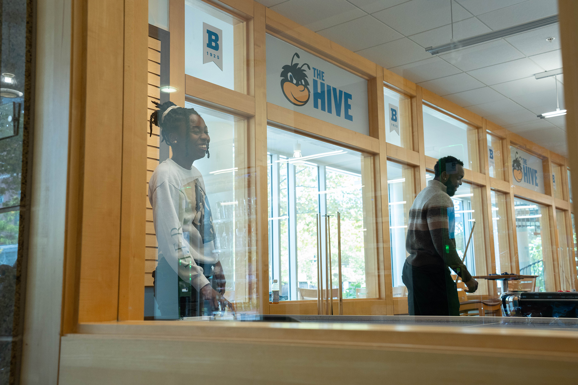 Seen through a window, a student smiles while playing air hockey