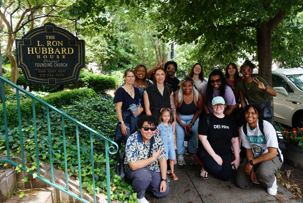 The class of students pose next to a sign at the front of the L. Ron Hubbard House.