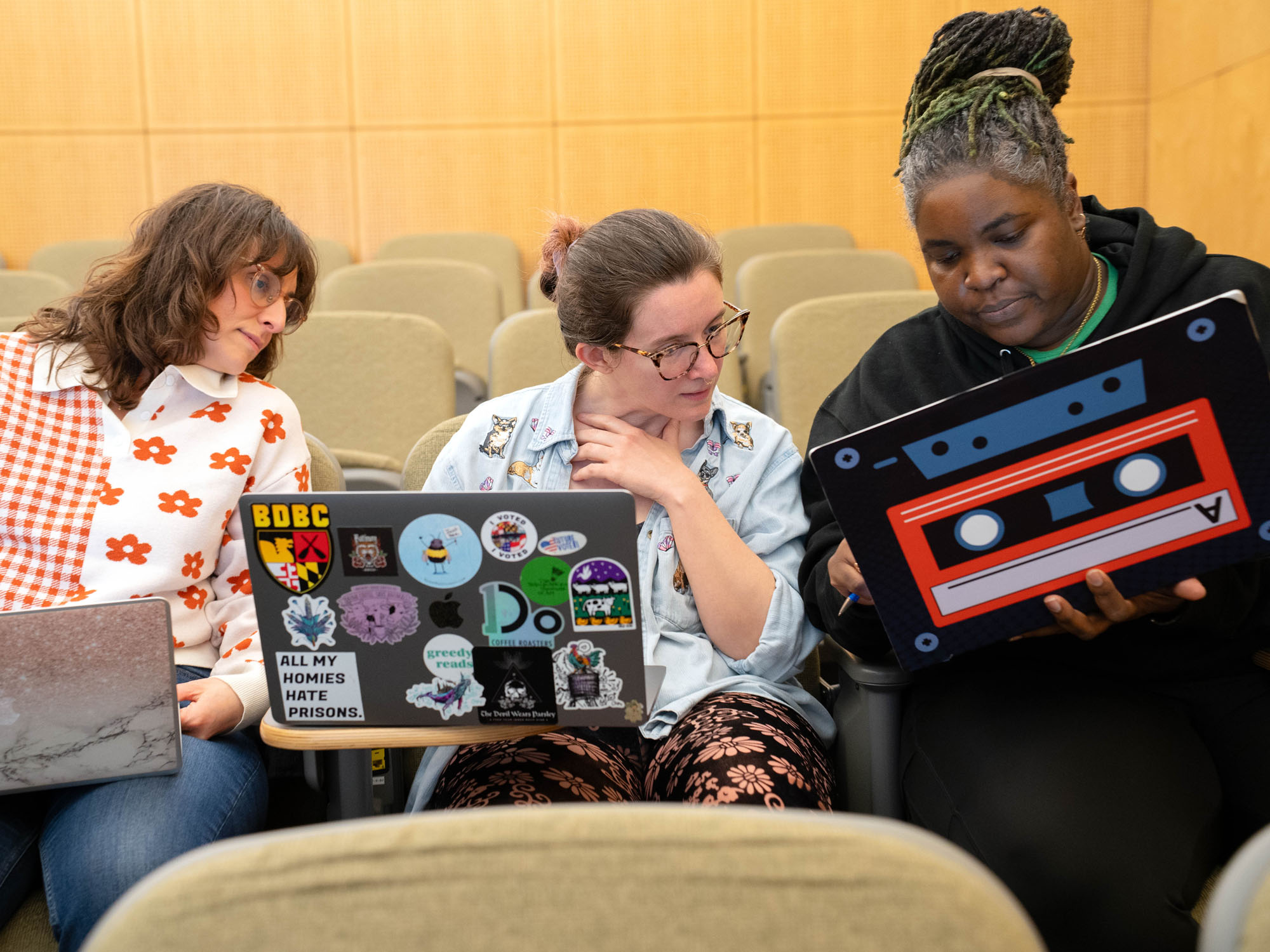 Three students, each with a laptop open, discuss a presentation while looking at one of the students' screens.