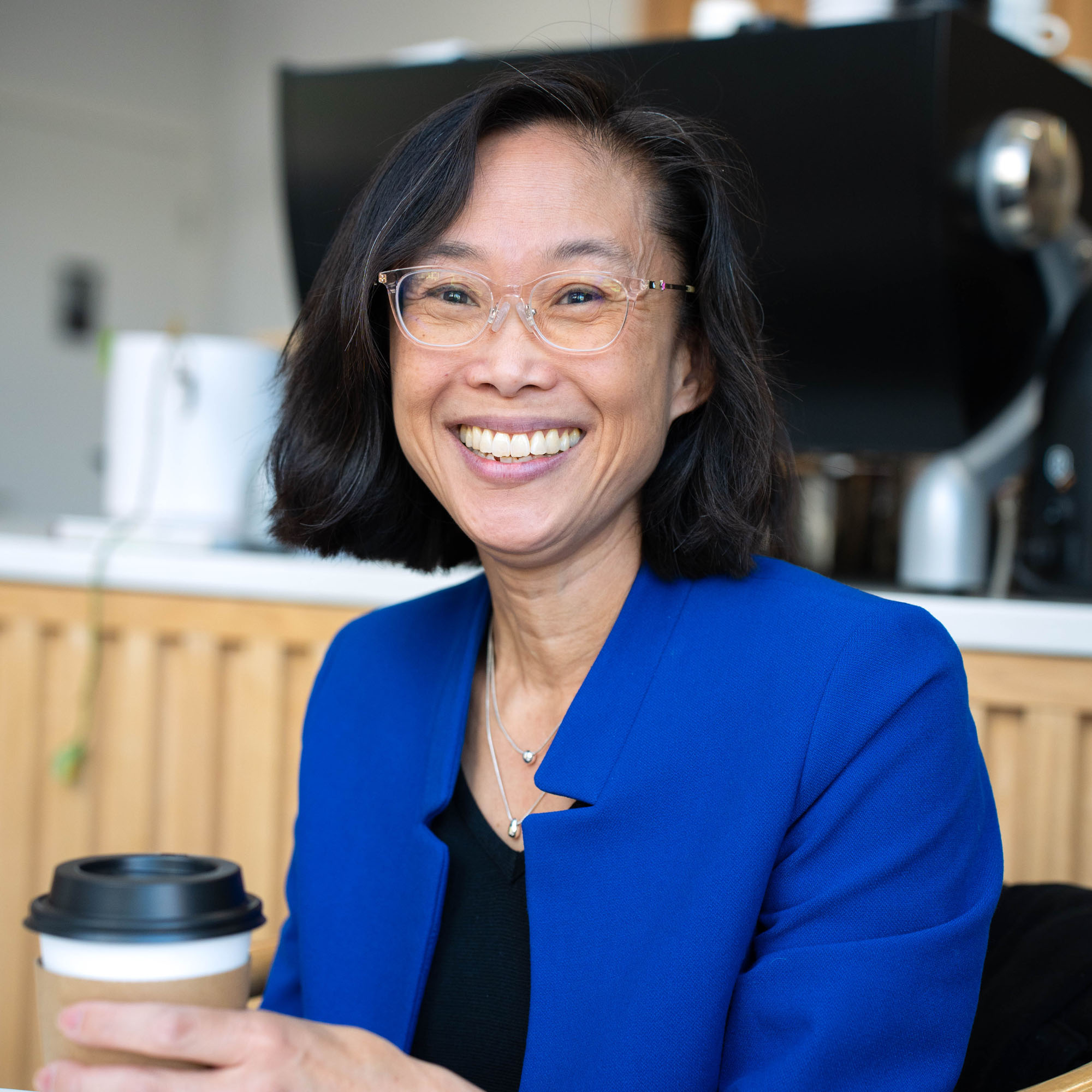 Jaime Lee smiles at the camera while holding a cup of coffee.