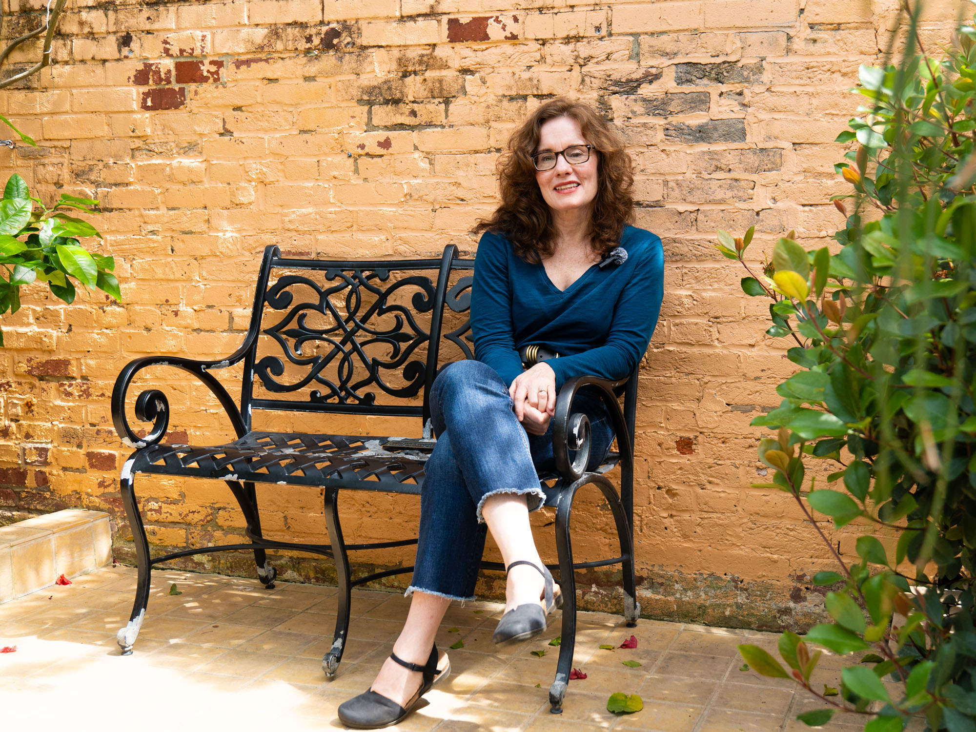 Jane Delury sits on an iron bench in front of a destressed brick wall