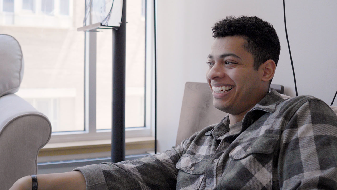 Judah looks on while laughing. He's sitting on a couch in the lounge at The Bob Parsons Centers Center at The University of Baltimore.