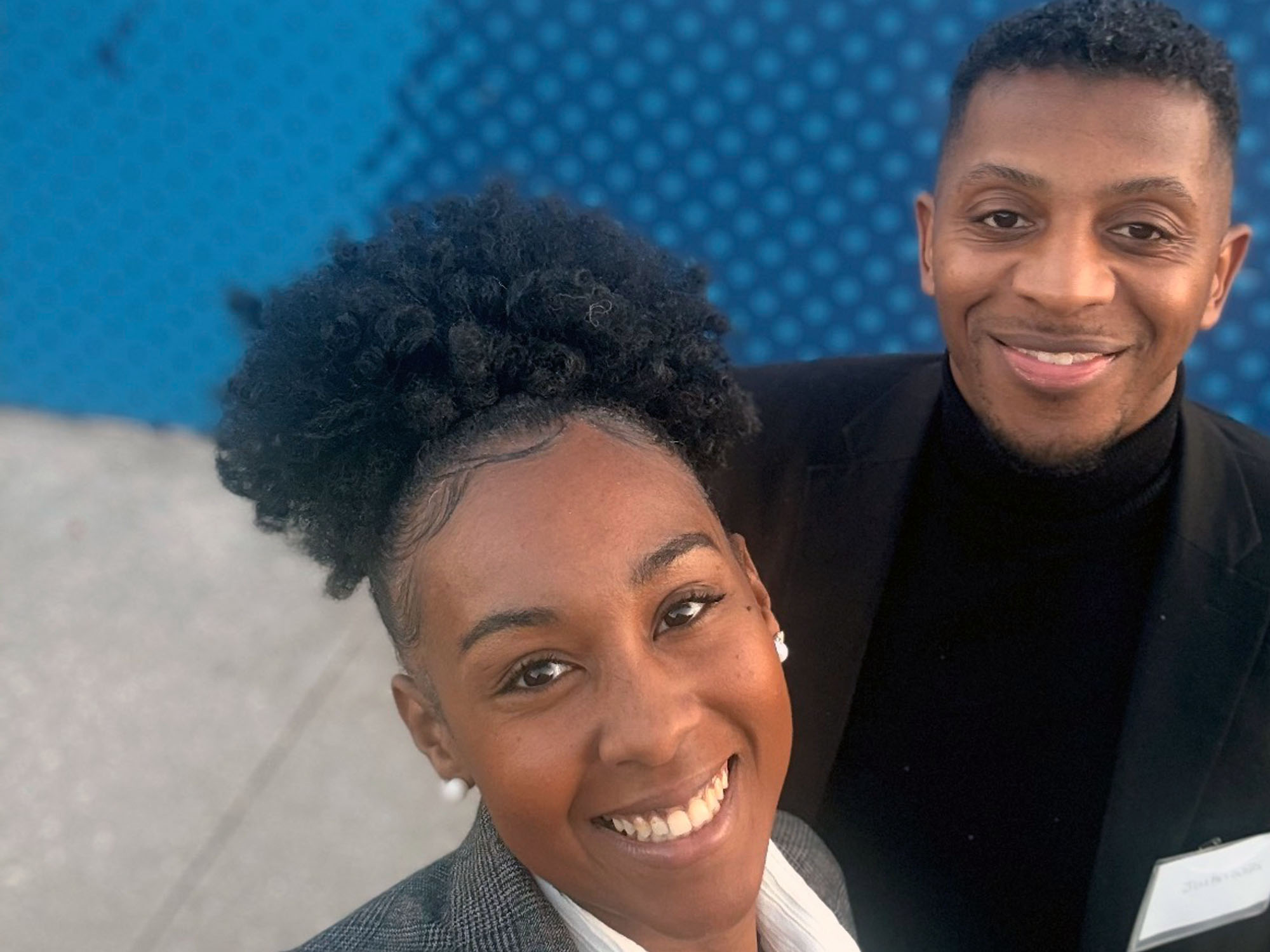 Natrea and Justin Wills pose for a selfie in front of a mural wall at The University of Baltimore.