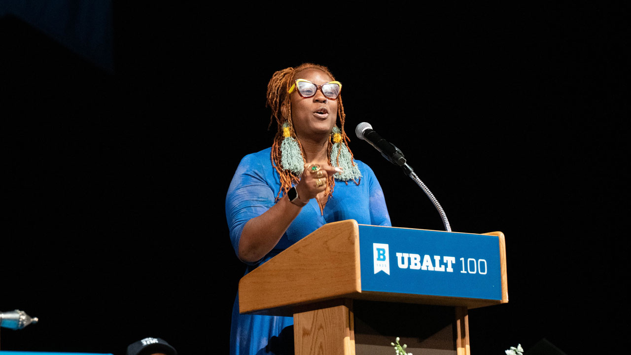Lady Brion performs a poem from a podium on stage.