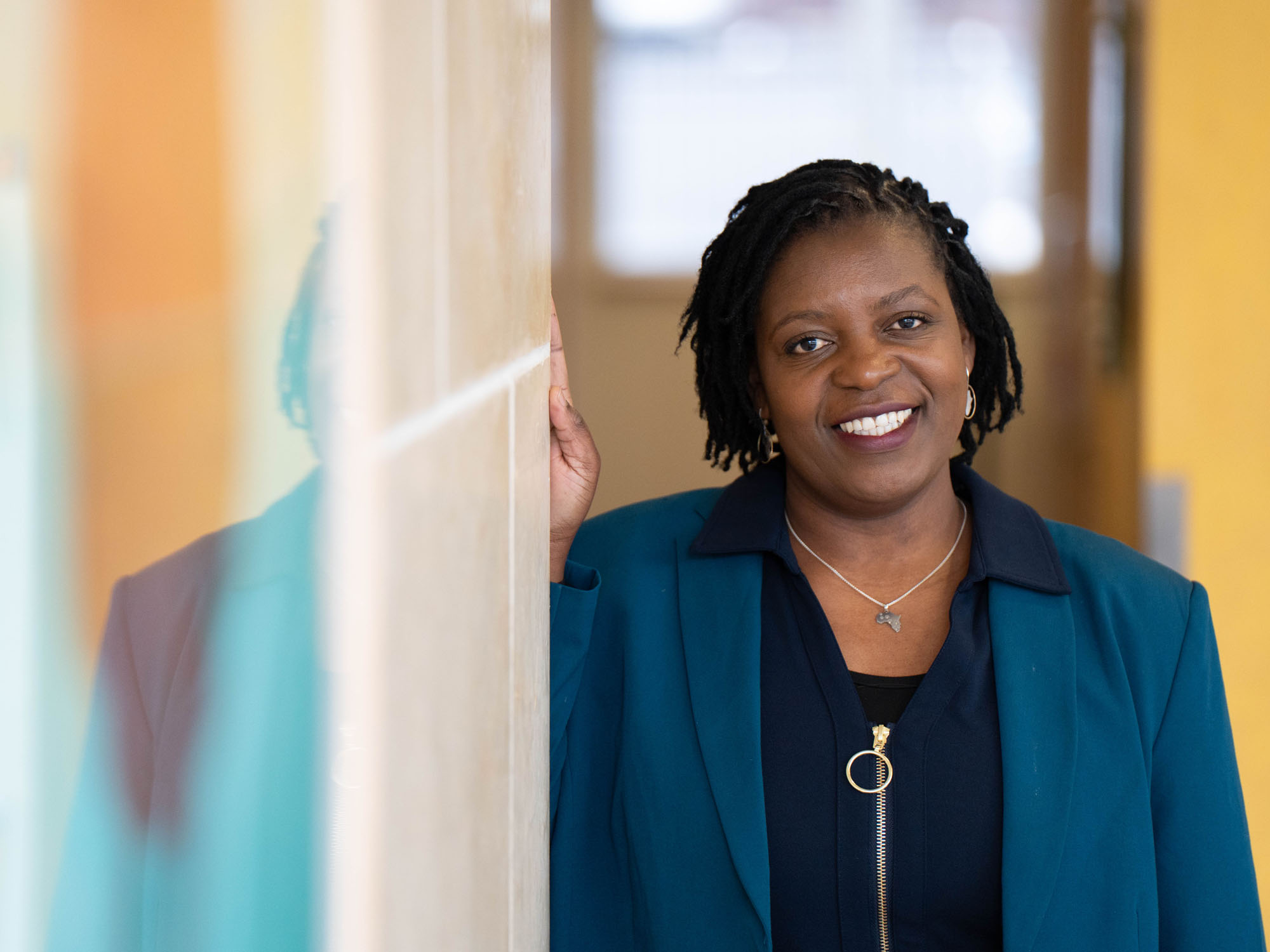 Memory Jakata smiles while looking at the camera. She's standing in the Student Center and leaning against a wall. Art hangs in the foreground.
