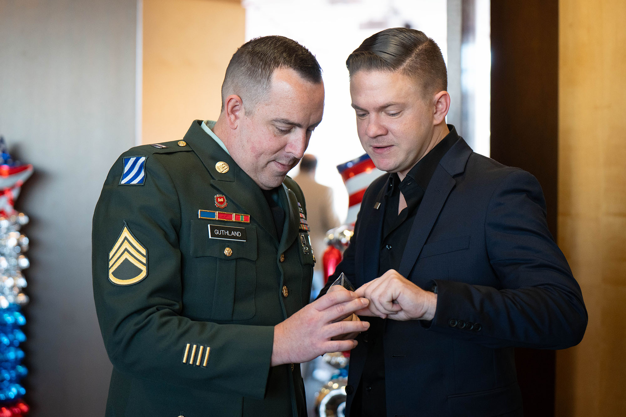 Michael Claxton shows a challenge coin to Josiah Guthland during the Veterans Day 2025 ceremony.