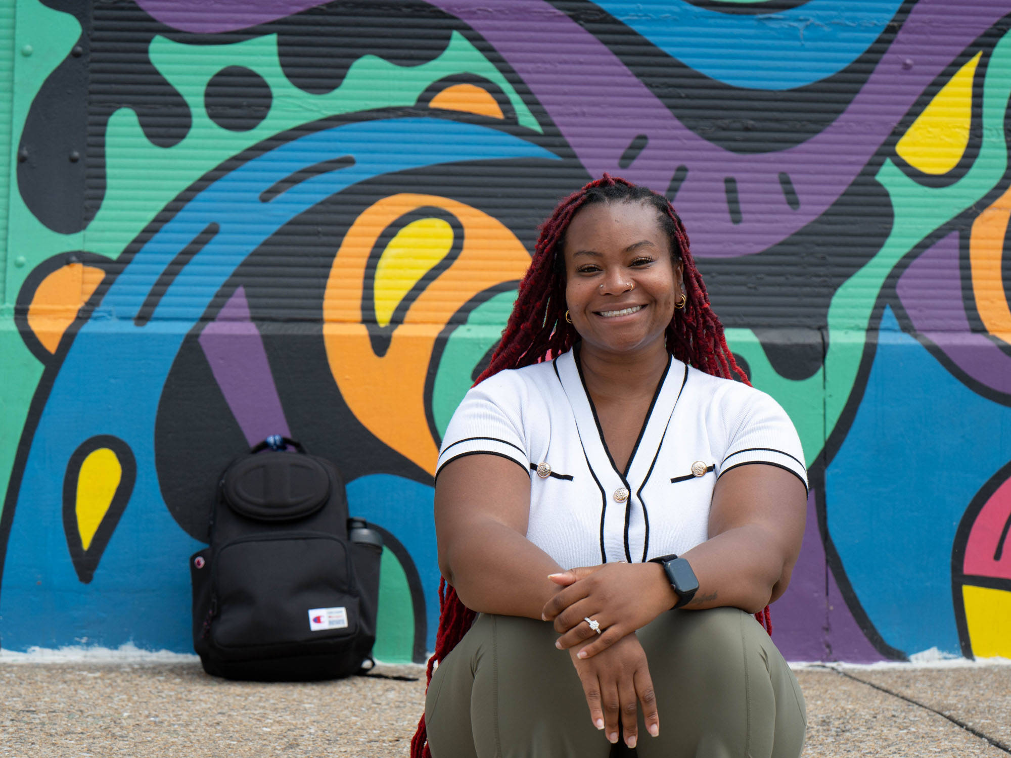 Nes, a UBalt student, smiles at the camera while sitting in front of colorful street art in Baltimore.