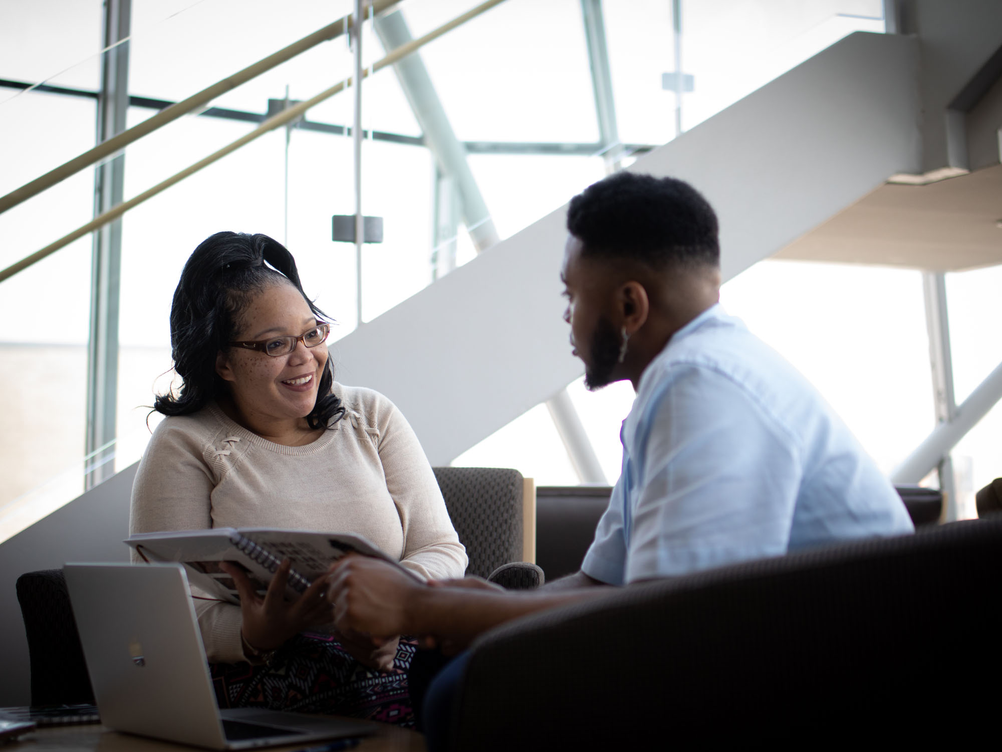Two students sit and talk in a building on campus.