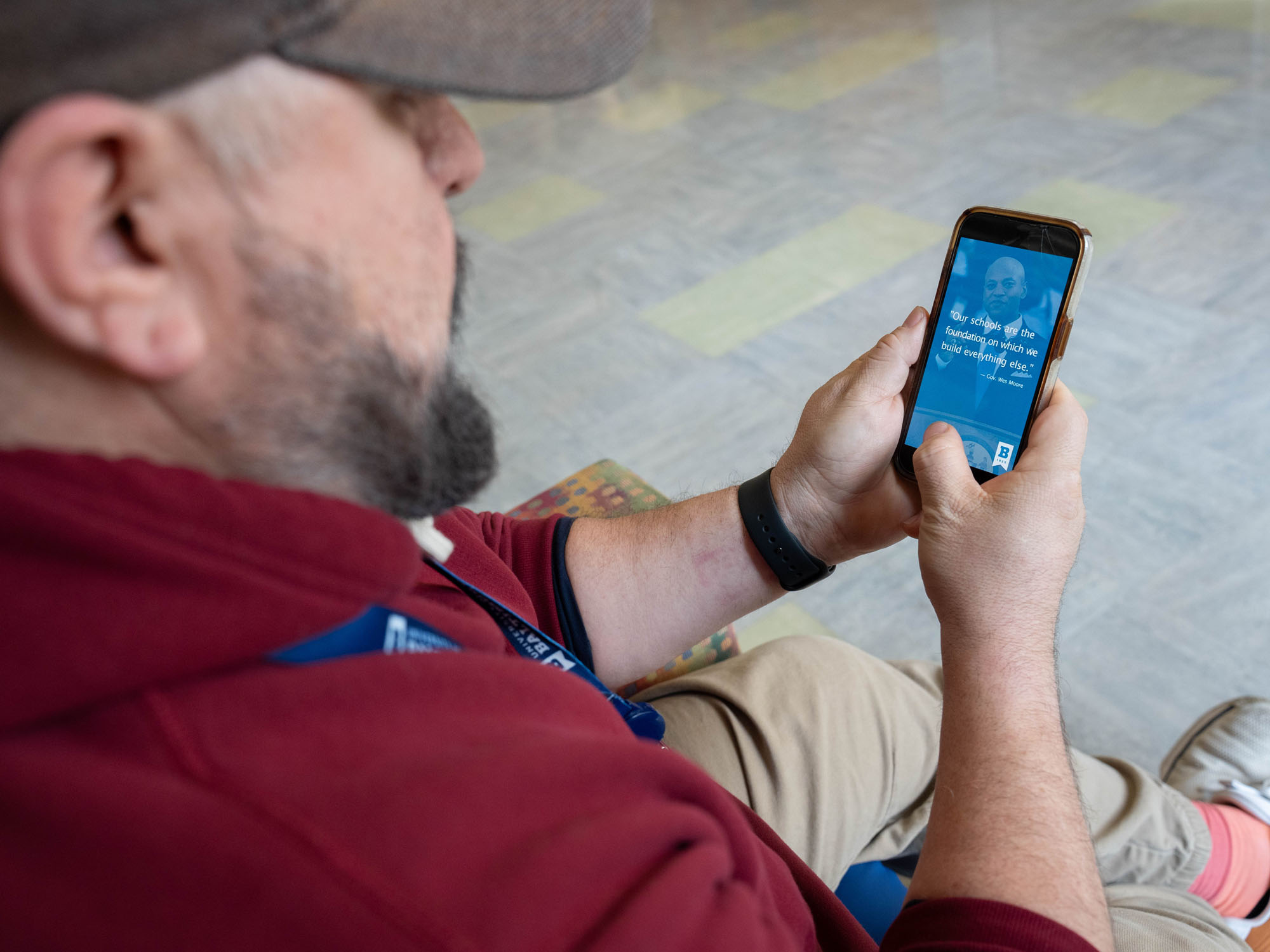 A male student wearing a ballcap looks at a smart phone to watch a Reel video.