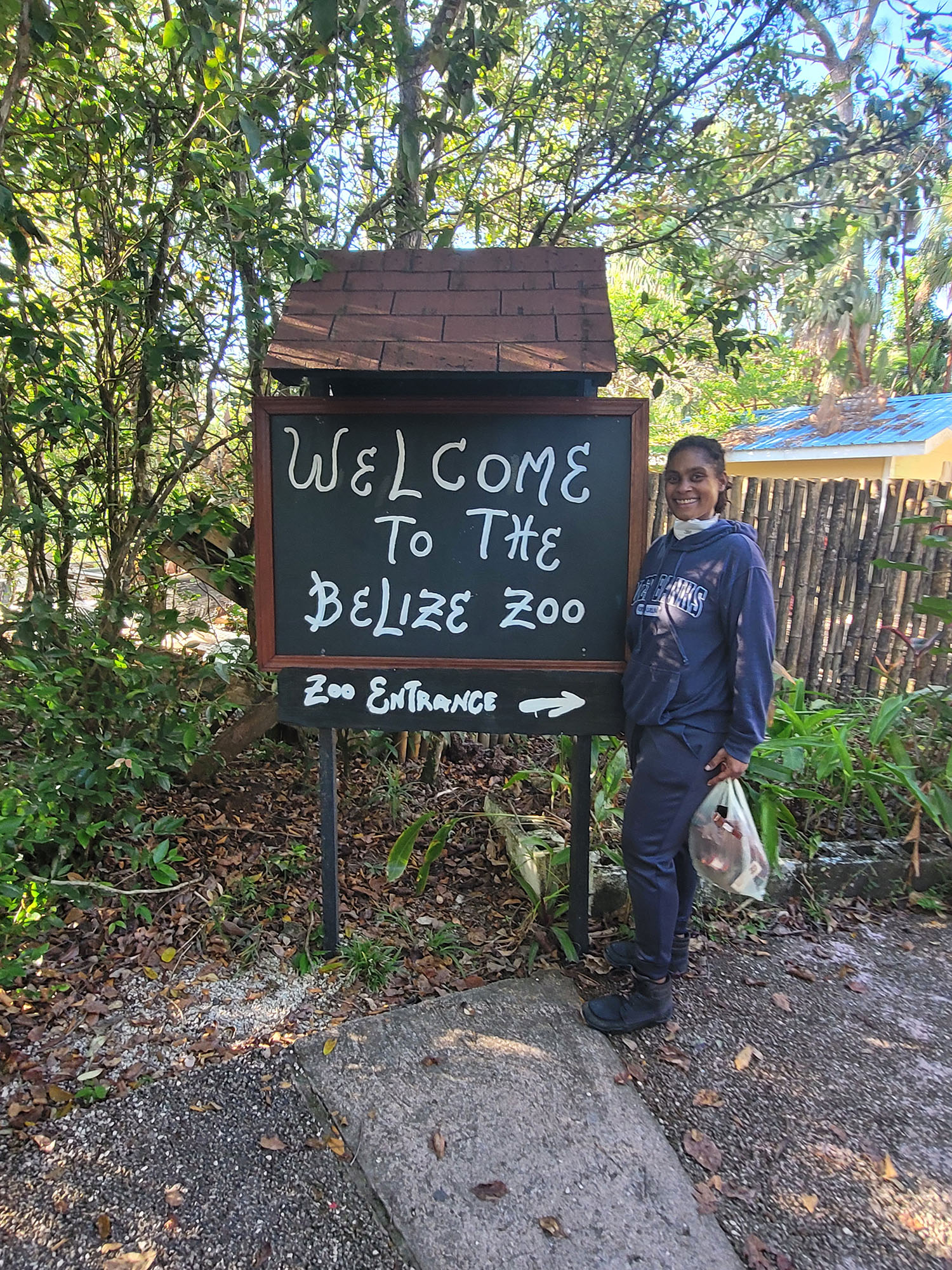 A student stands next to a welcome sign in Belize. 