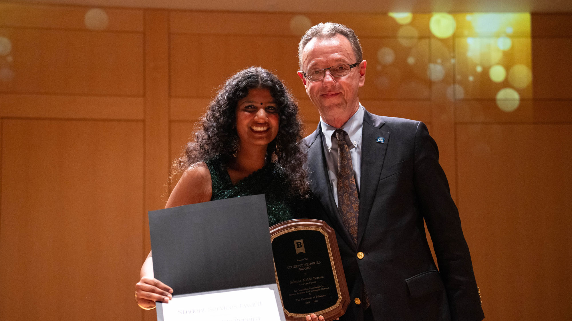 A student poses at an award ceremony with her award and certificate with the award presenter.