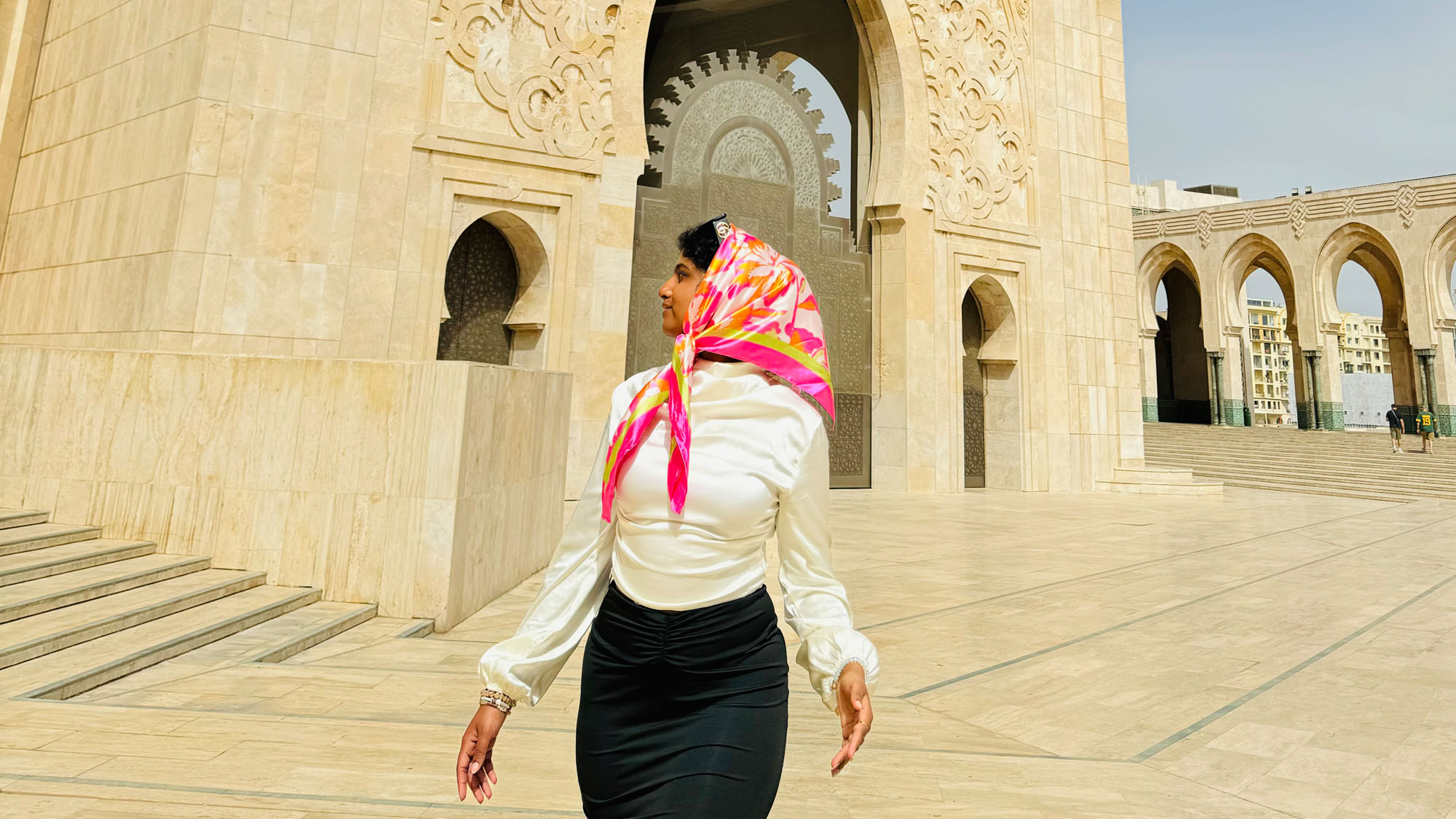 A student wearing a brightly colored scarf looks around her while standing in a public square in Morocco.