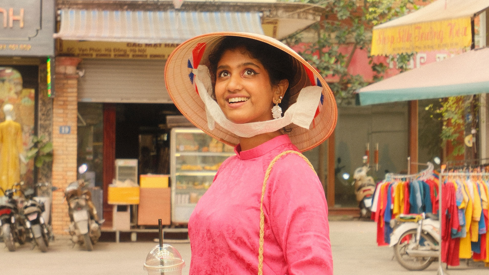 A student wearing a hat observes an outdoor market in Vietnam.
