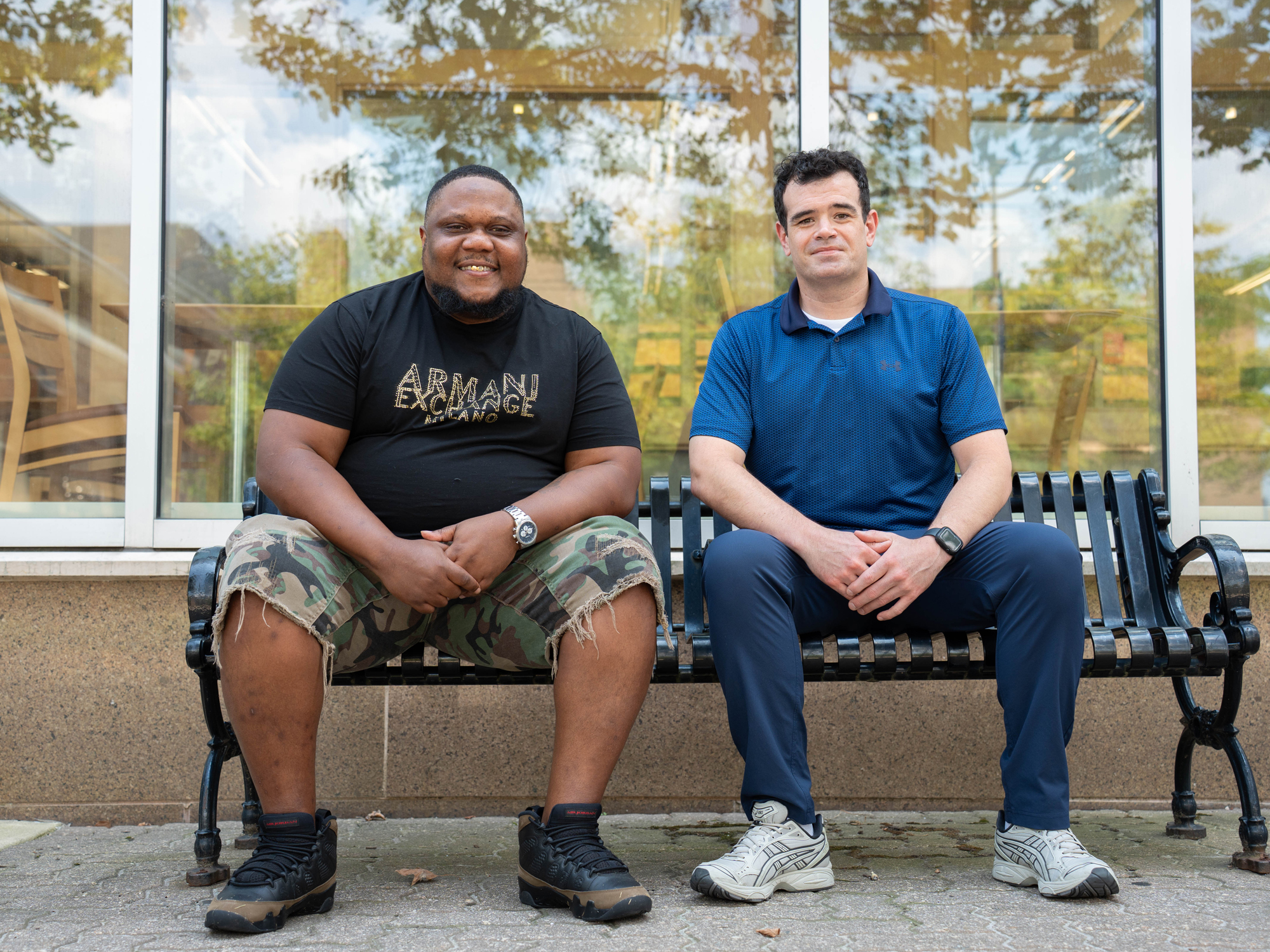 Two students sit on a bench on campus.