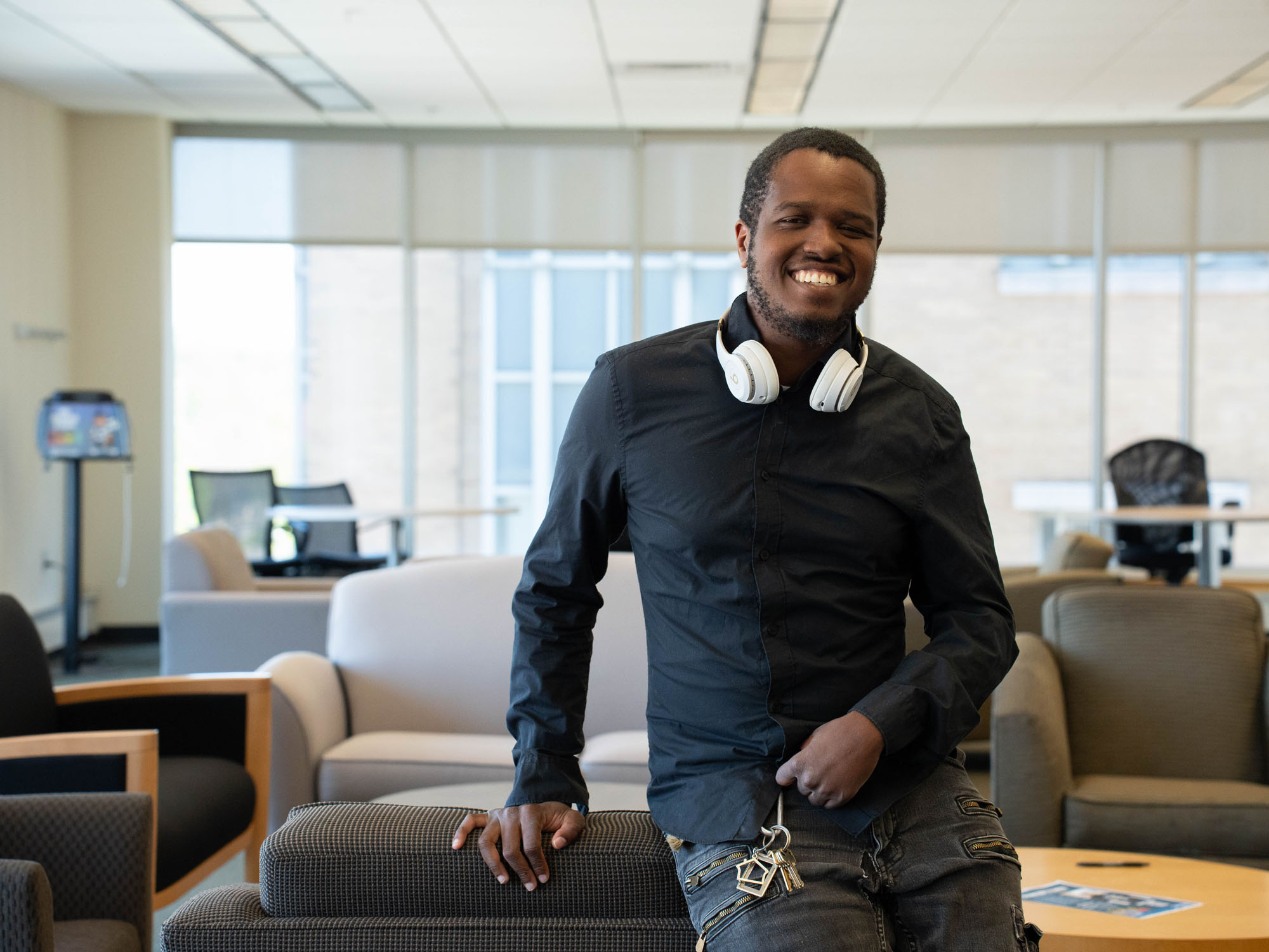 A student wearing headphones around his neck poses for a photo in a lounge.