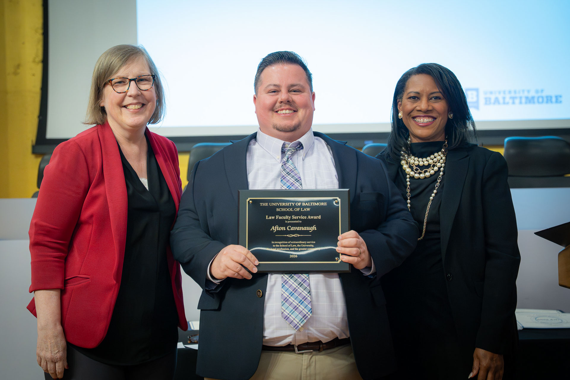Three people pose during a University of Baltimore School of Law awards ceremony, with one recipient holding an award plaque.