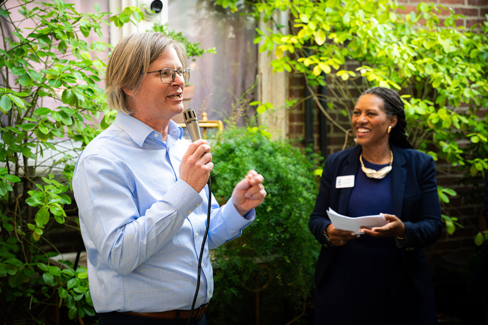 A speaker addresses attendees with a microphone during an outdoor UBalt Law alumni event.