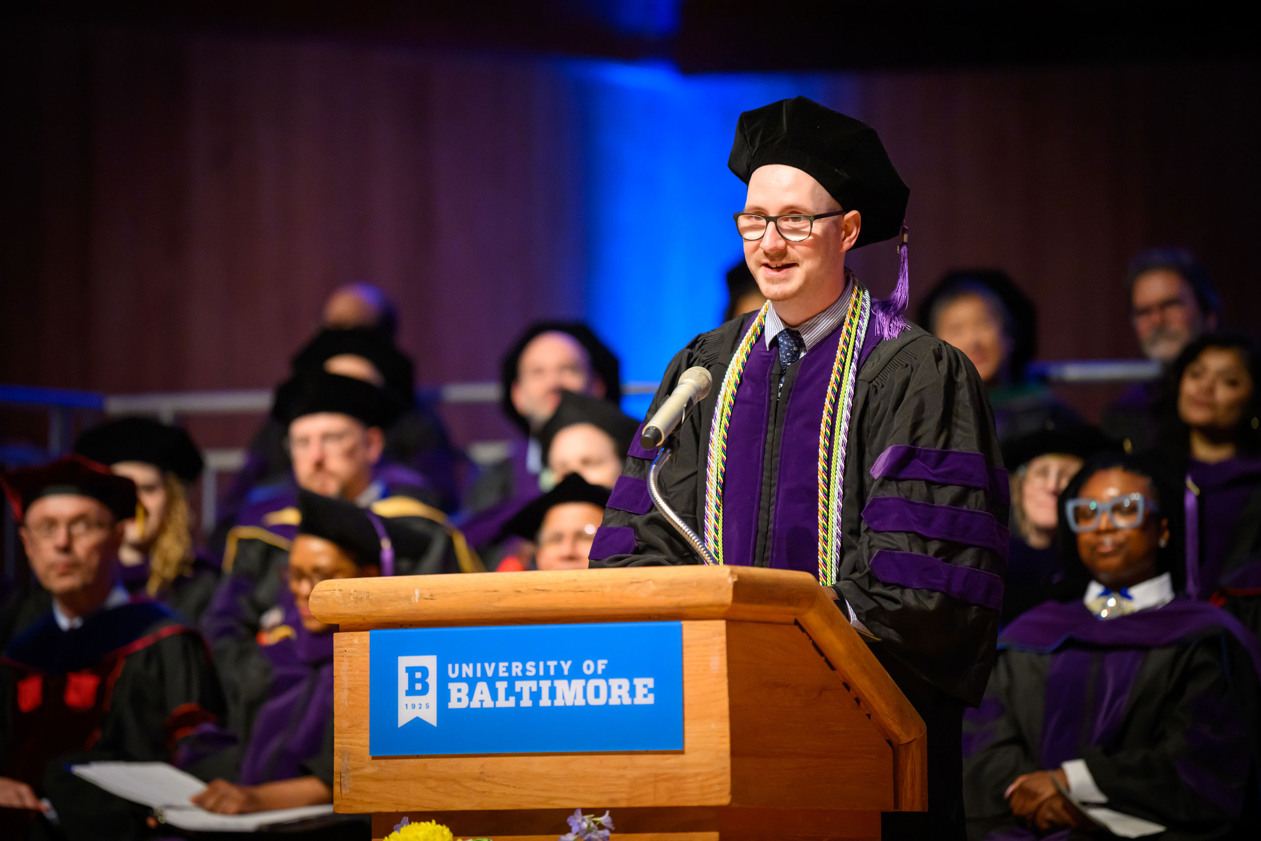A valedictorian in academic regalia speaks at the podium during the University of Baltimore School of Law commencement ceremony.