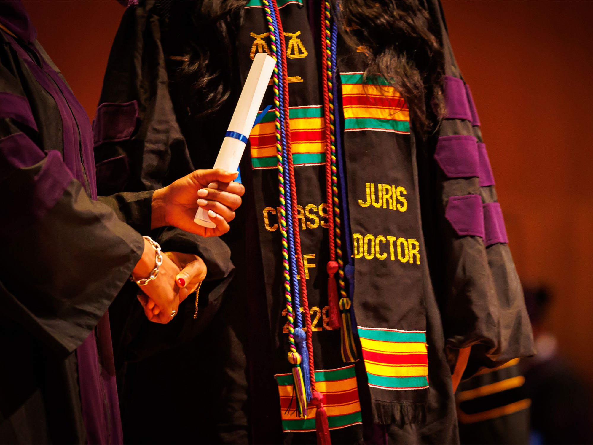 A graduate wearing academic regalia and honor cords holds a diploma during the University of Baltimore School of Law commencement ceremony.